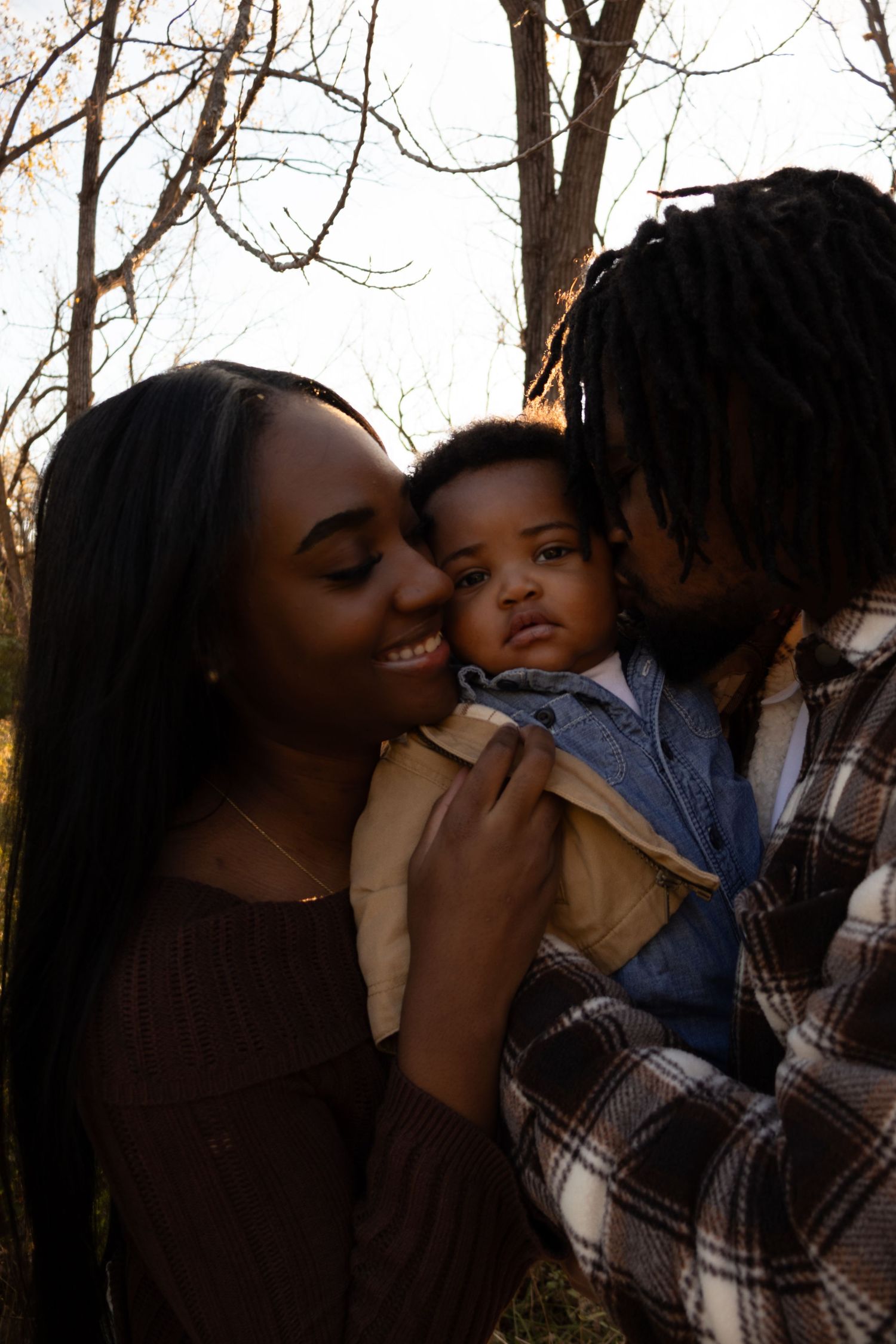 A family shares an intimate moment together outdoors during golden hour as bare tree branches frame the scene.
