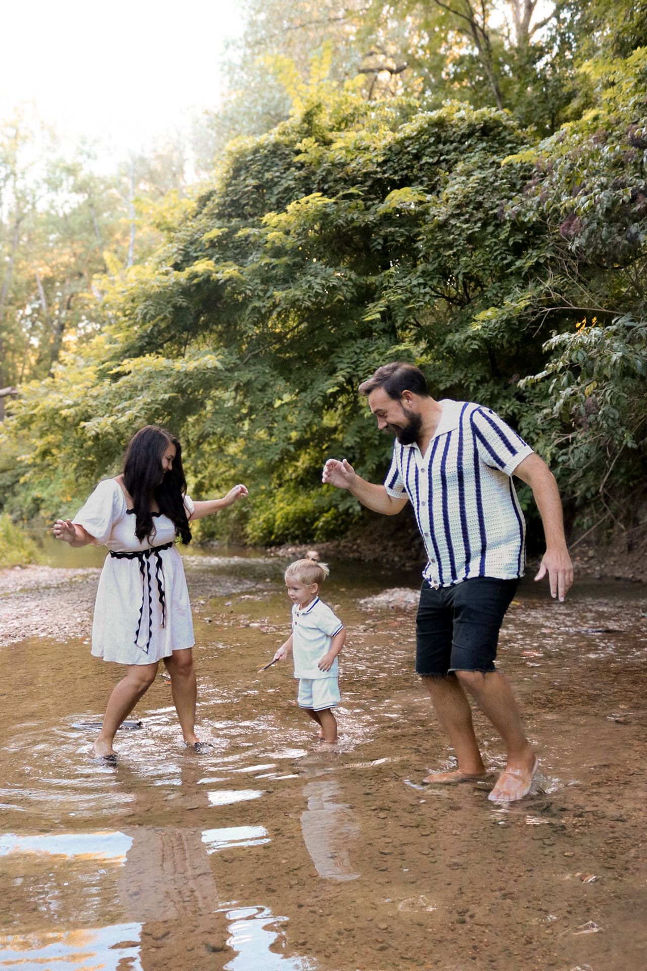 Family playing and splashing in shallow creek water on sunny day.