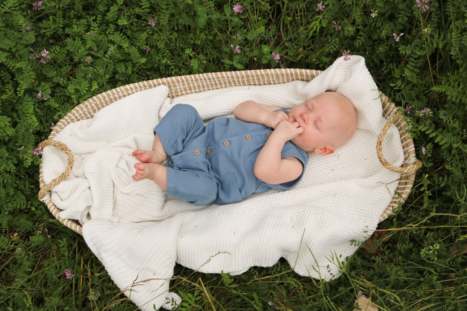 Infant sleeping peacefully on white blanket outdoors in nature.