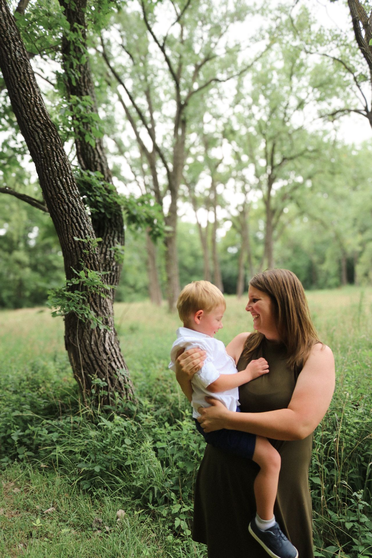 A tender family moment captured under a large tree in a lush green setting.