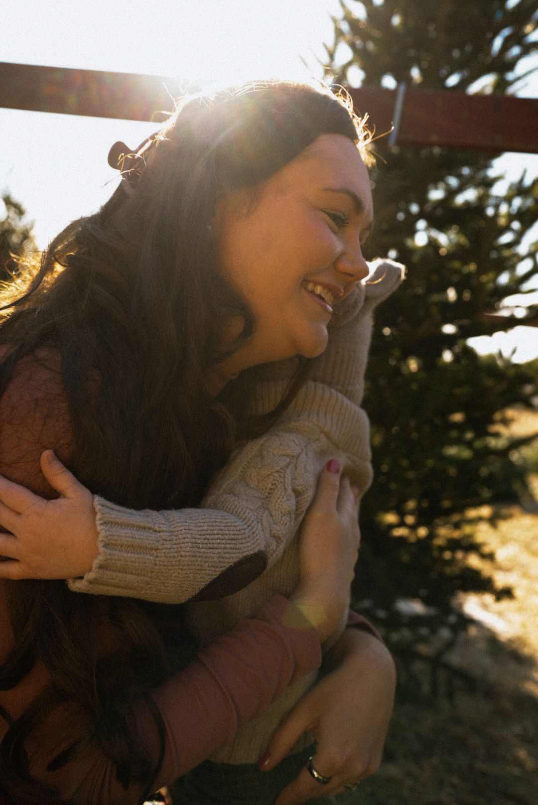 Person in a sweater enjoying a warm sunset moment with lens flare and natural backlighting through trees.