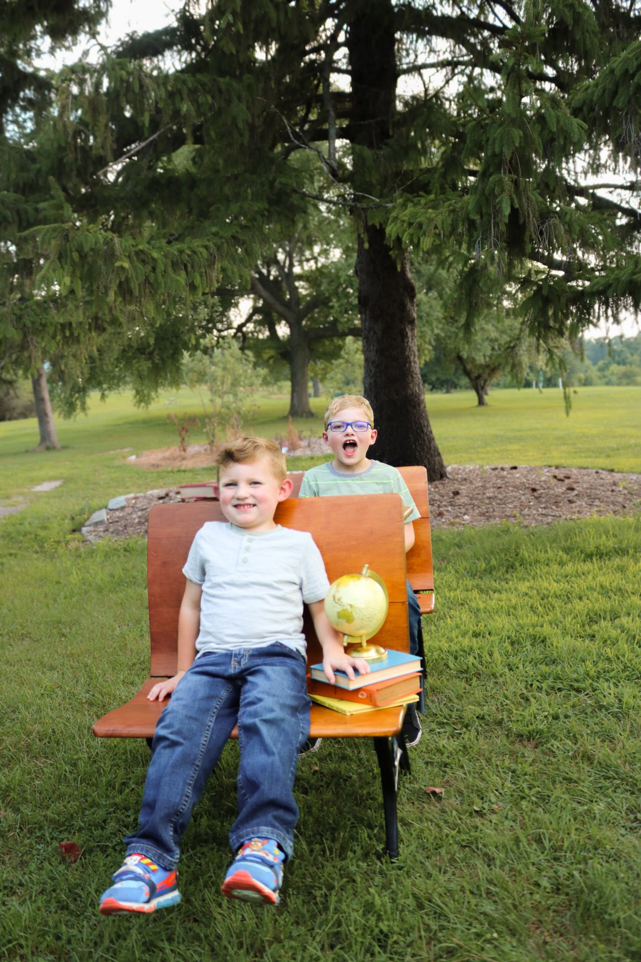 Child relaxing on orange park bench surrounded by green trees.