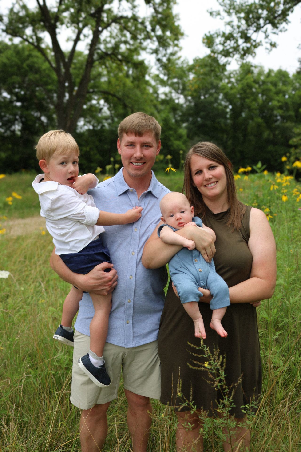 A family portrait taken outdoors in a meadow with tall grass and yellow flowers in the background.
