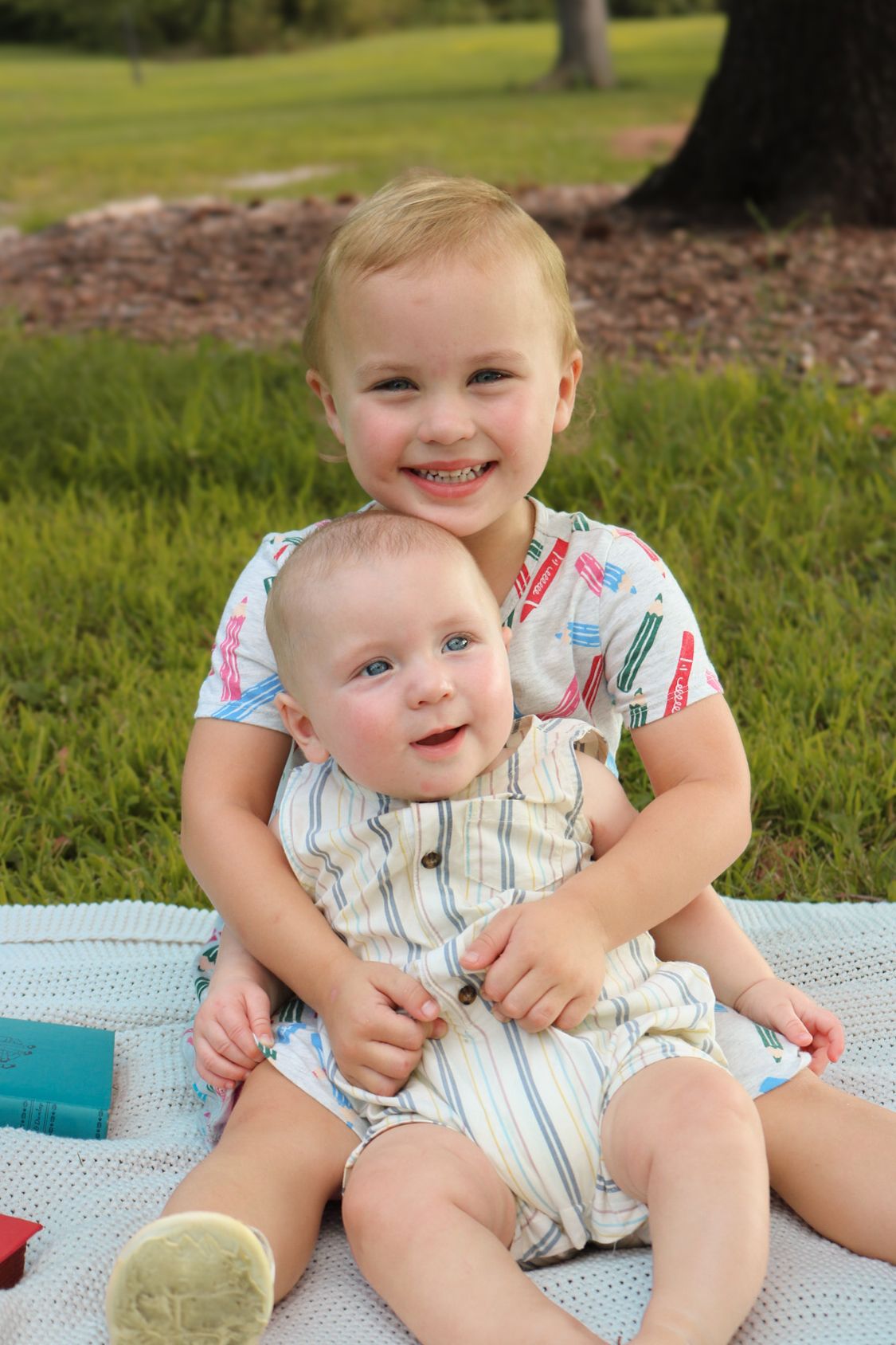 Two small children sharing a sweet moment on a picnic blanket outdoors.