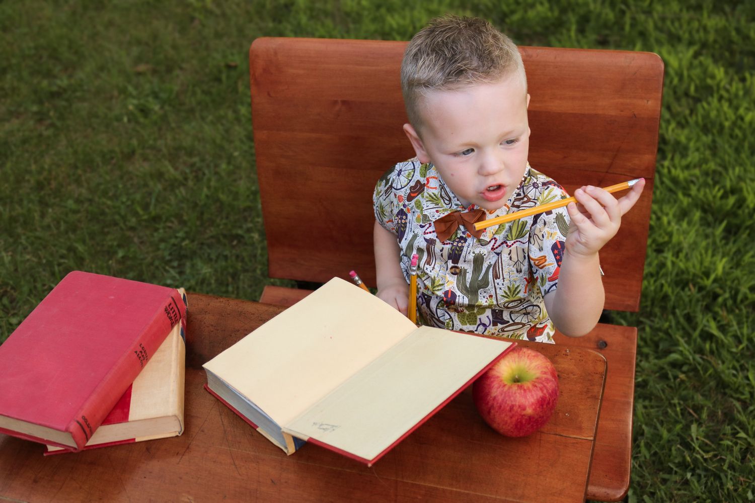 Child reading a book with an apple and globe on a wooden bench outdoors.