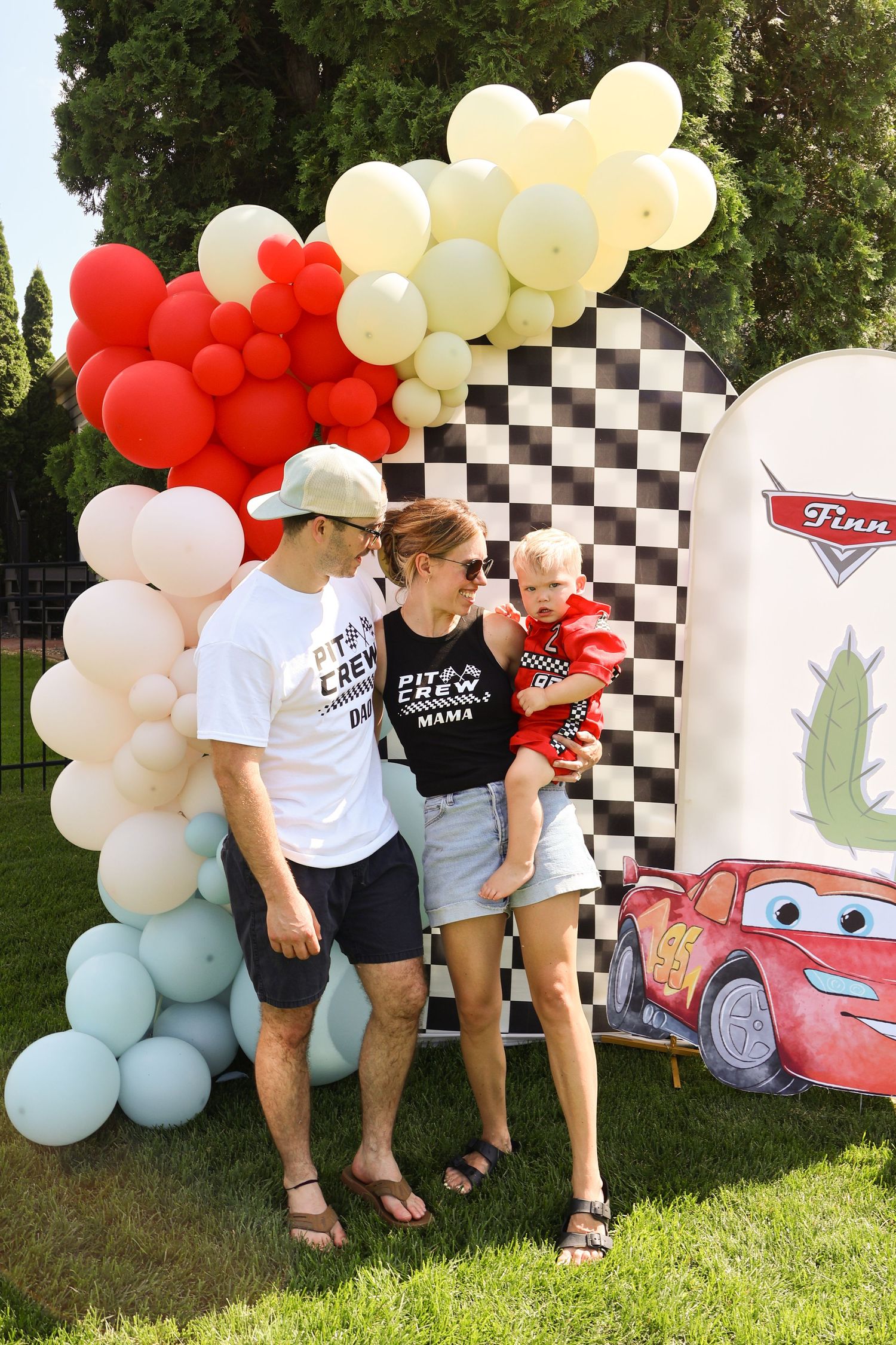 Cars themed party setup with red and white balloon arch and checkered backdrop.