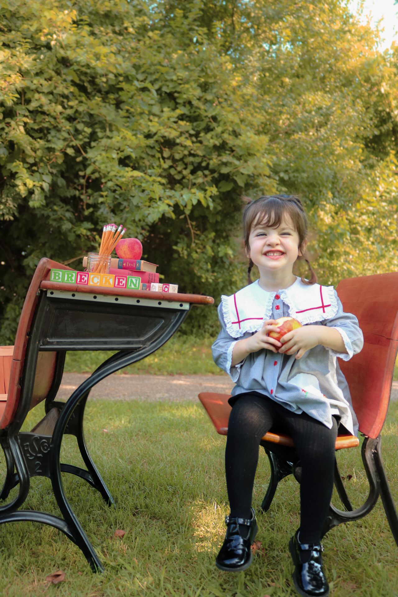 Child reading colorful books while sitting on a vintage red bench in a park setting during autumn.