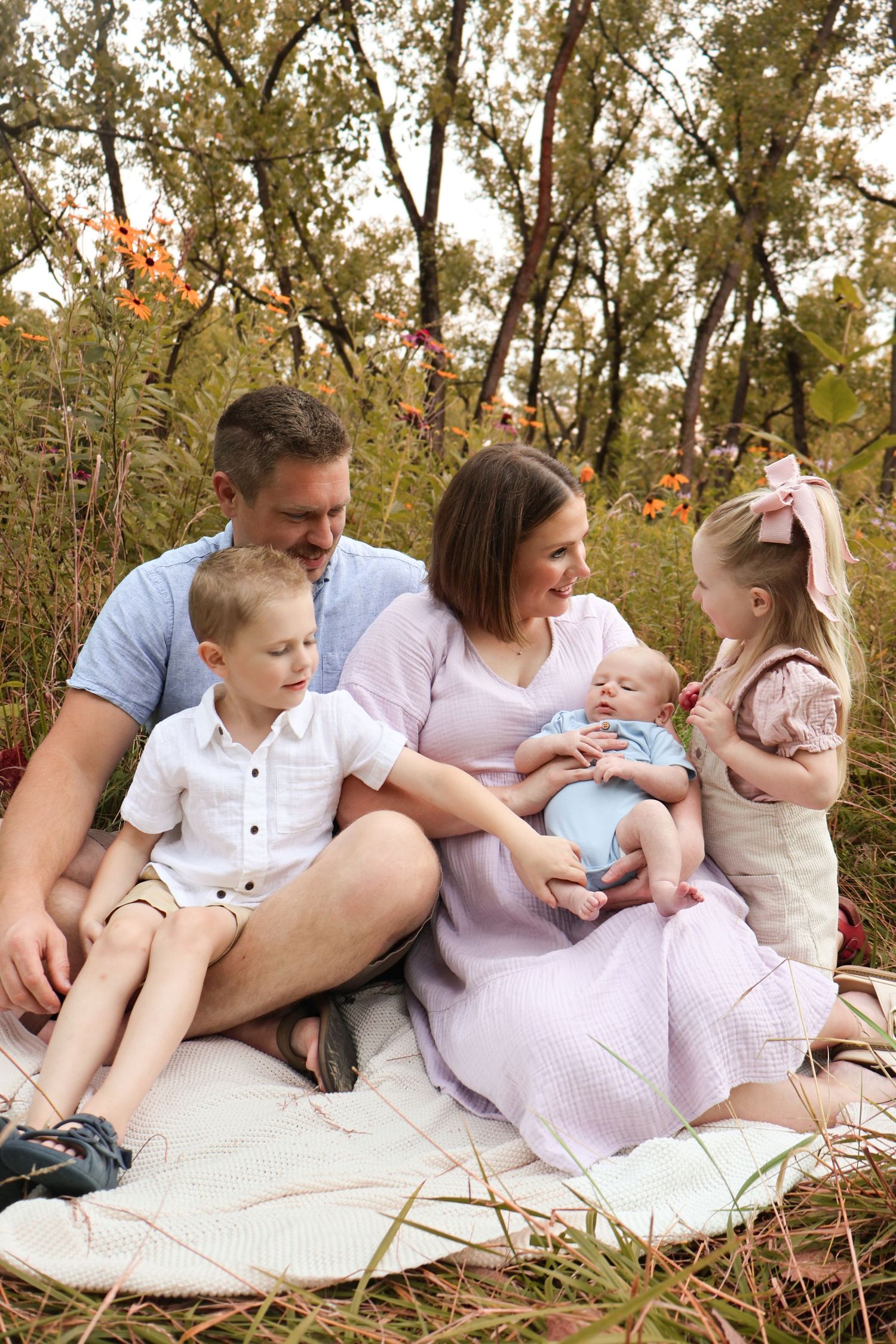 Family relaxing together on a white blanket during an outdoor photo session in nature.