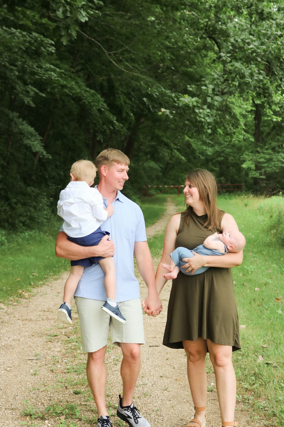 A family walks hand in hand down a shaded forest trail on a summer day.