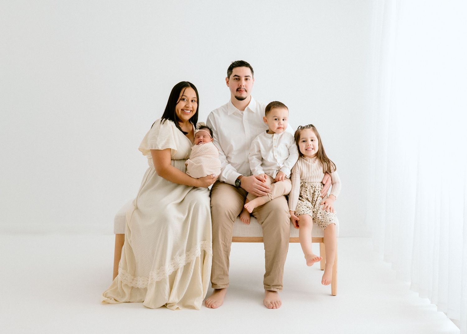 Family wearing neutral colors poses together on white backdrop for minimalist portrait.
