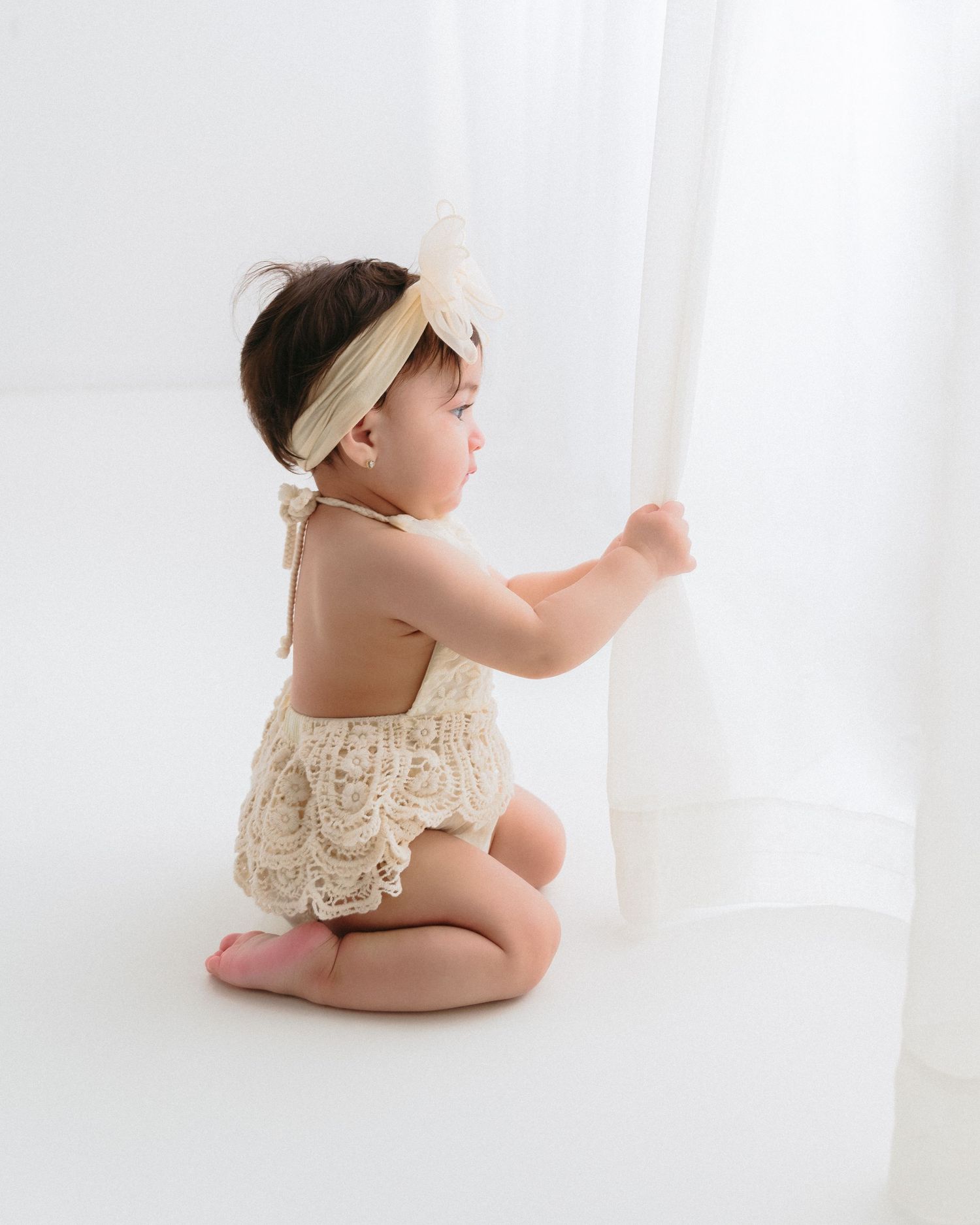 Baby in lace outfit sitting against white backdrop. Appleton, Green Bay & Kaukauna