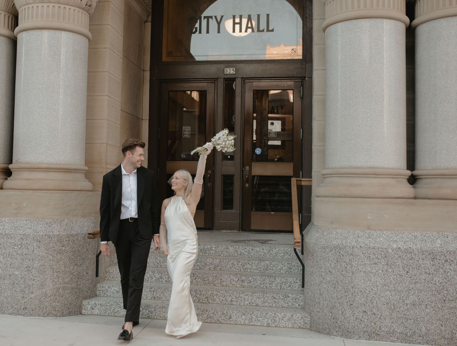 Couple in formal attire walking up stairs at City Hall entrance.