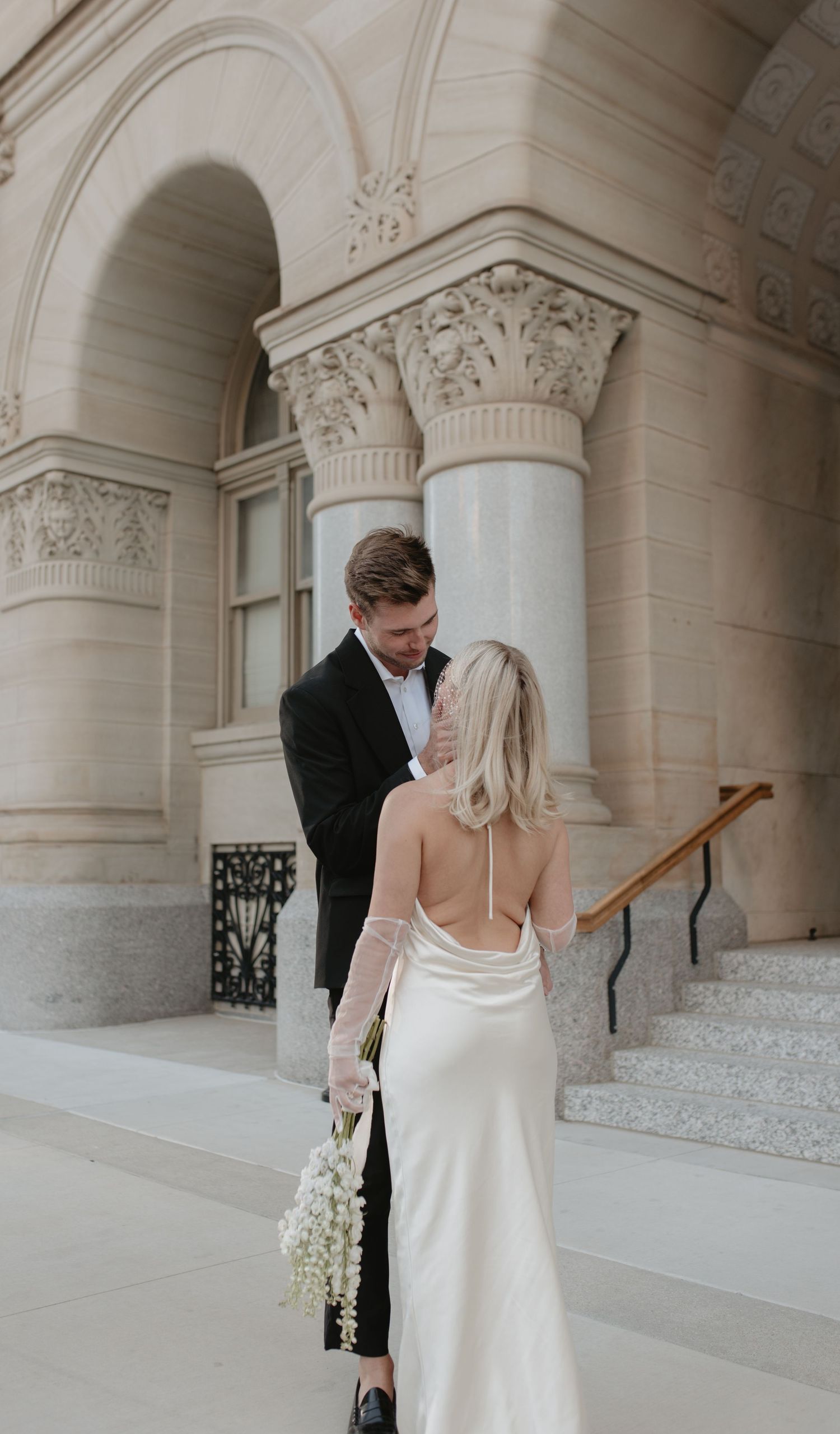 Elegant wedding couple embracing near classical stone columns and architectural details.