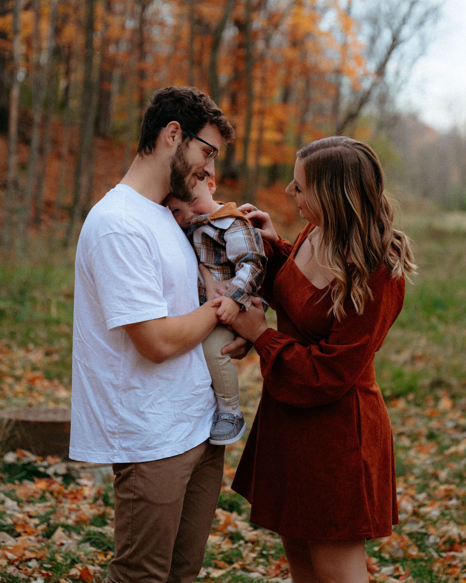 A family plays together among fallen autumn leaves during an outdoor photoshoot.