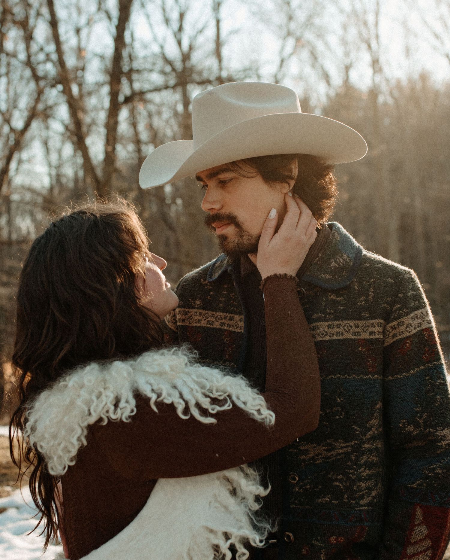 Romantic western-themed photoshoot in a wooded setting with cowboy hat and rustic attire.