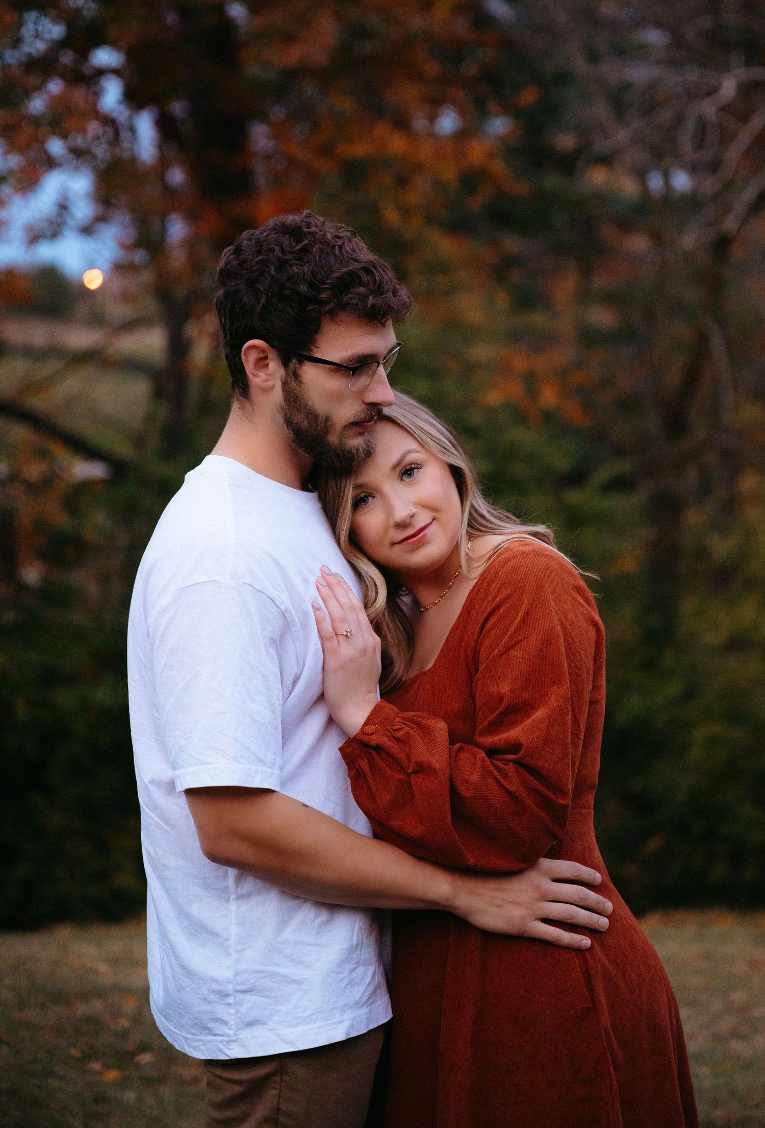A romantic autumn portrait with orange fall foliage in the background during sunset.