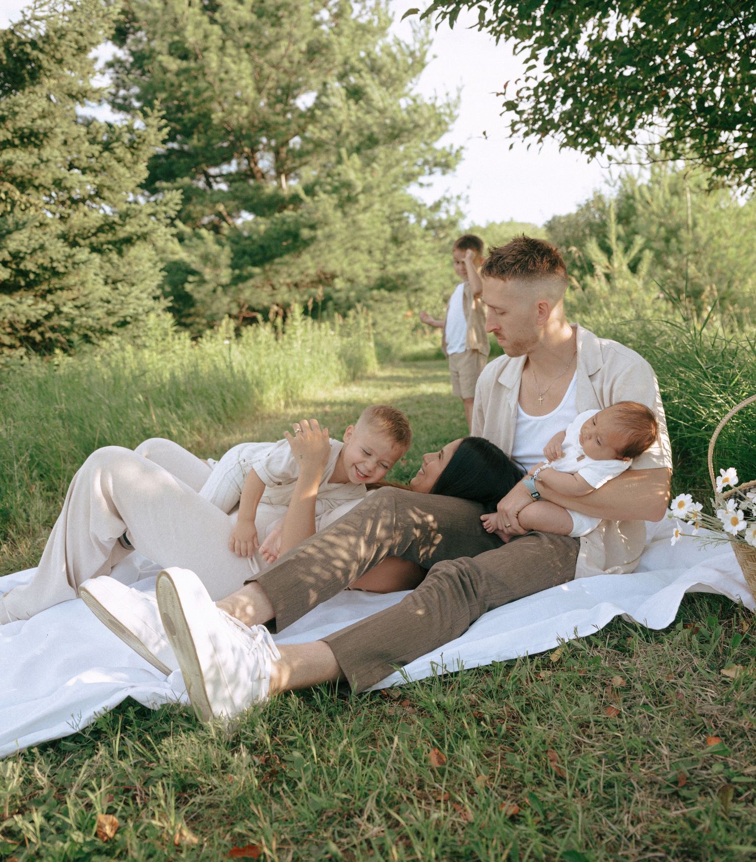 Family lying together on a blanket in grass during a sunny outdoor photo session.