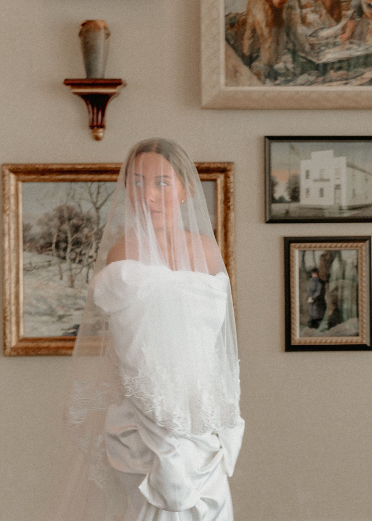 Wedding dress and veil hanging in a room with framed artwork on beige walls. Appleton, Green Bay & Kaukauna