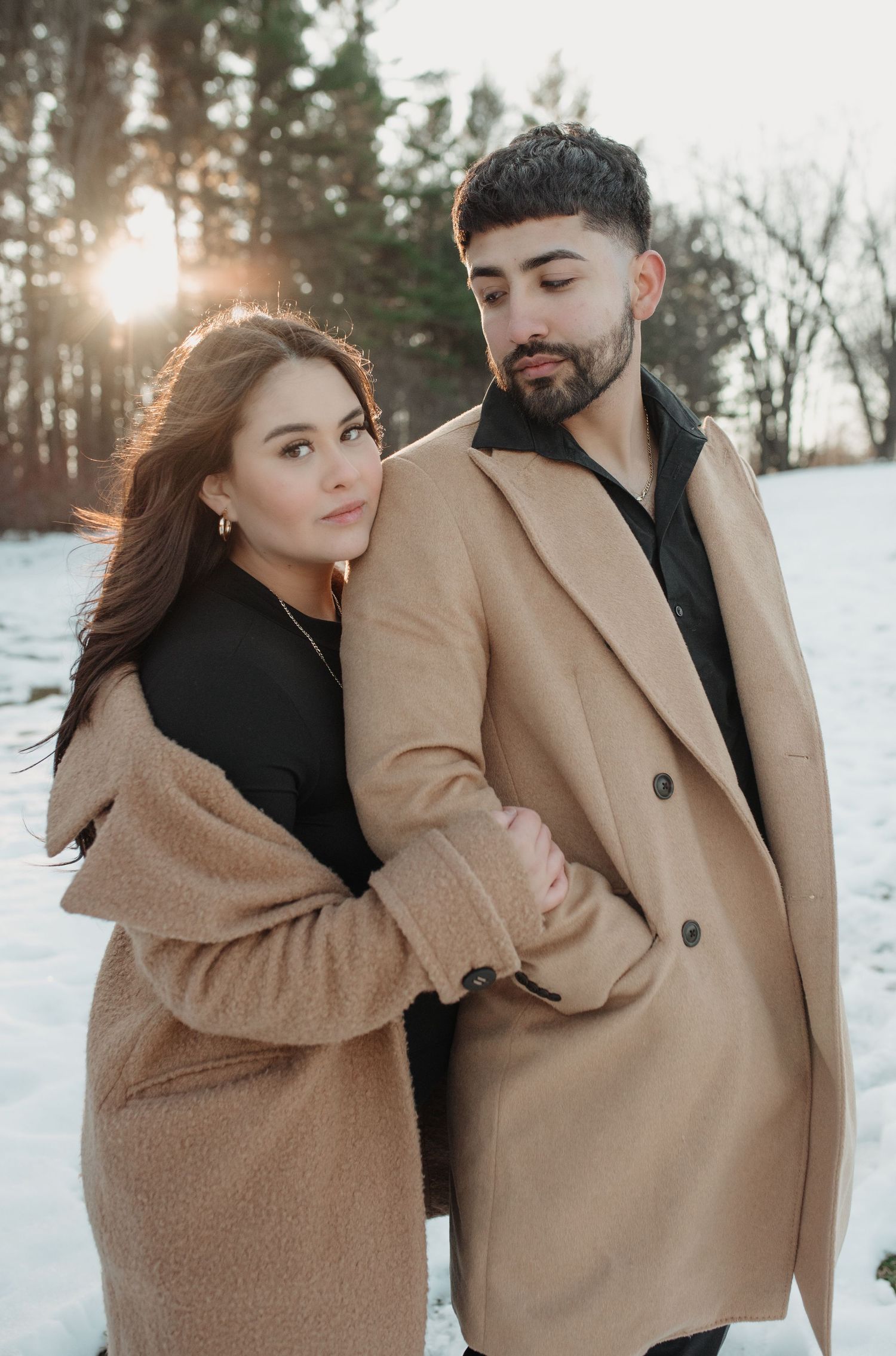 Playful winter photoshoot featuring couple in coordinated tan and black outfits against snowy landscape. Appleton, Green Bay & Kaukauna