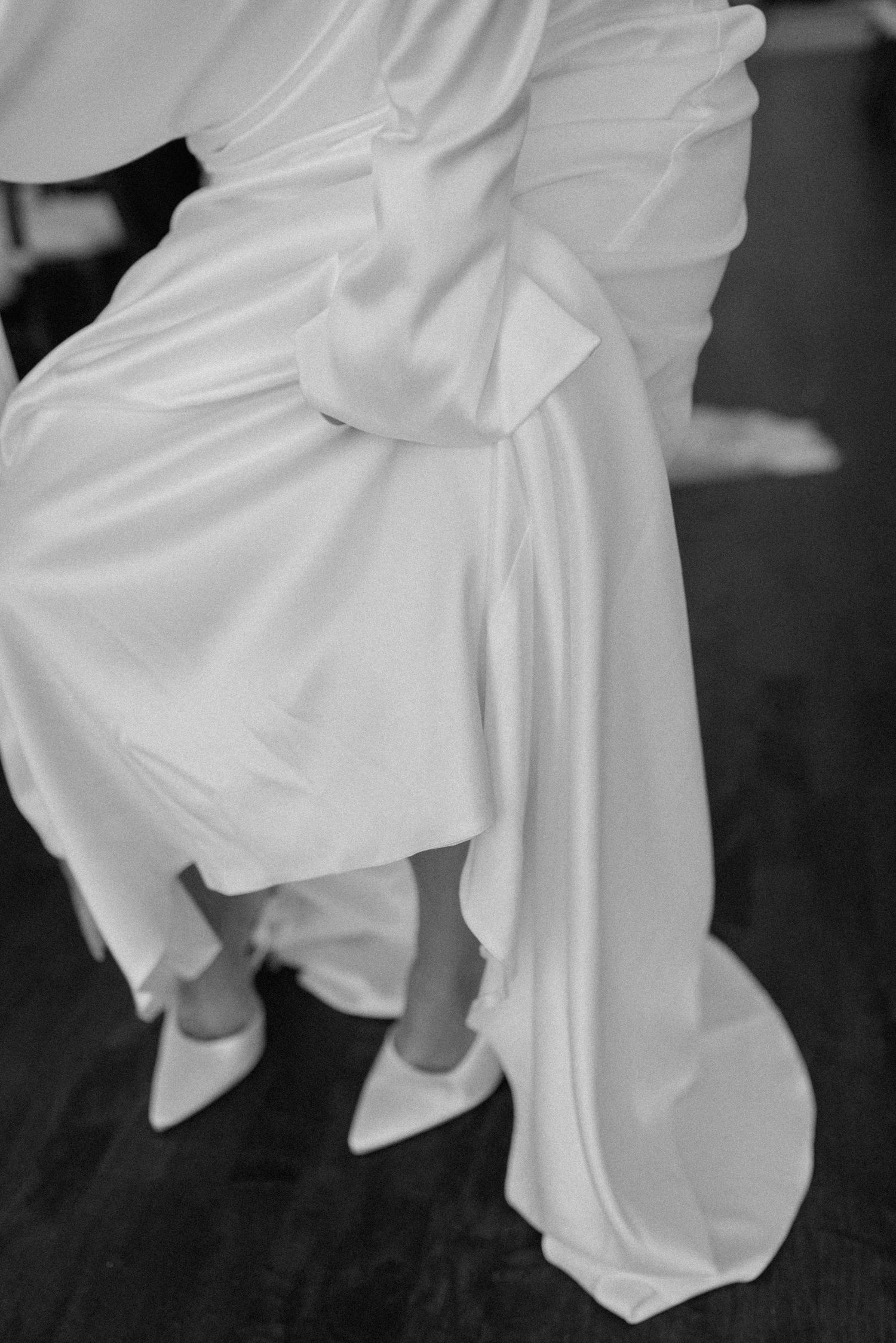 Close-up detail shot of flowing white wedding dress fabric against dark wooden flooring.