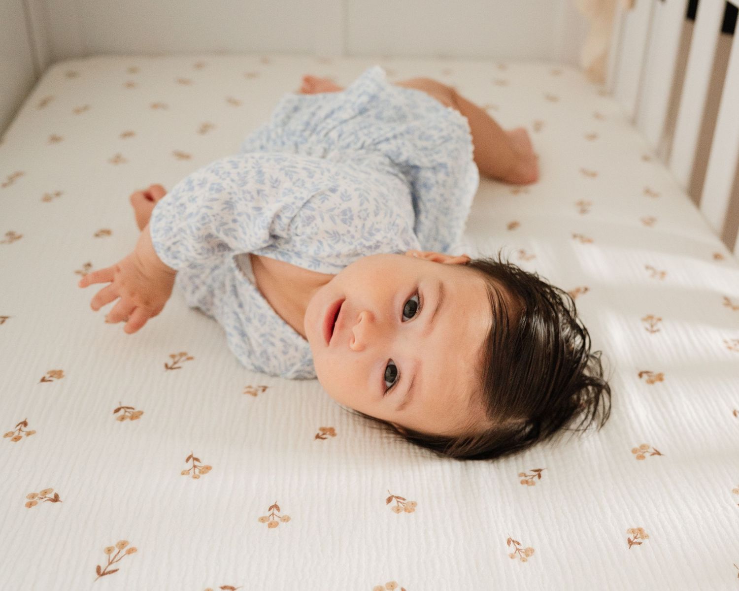 Infant lying on floral patterned mattress wearing grey outfit. Appleton, Green Bay & Kaukauna