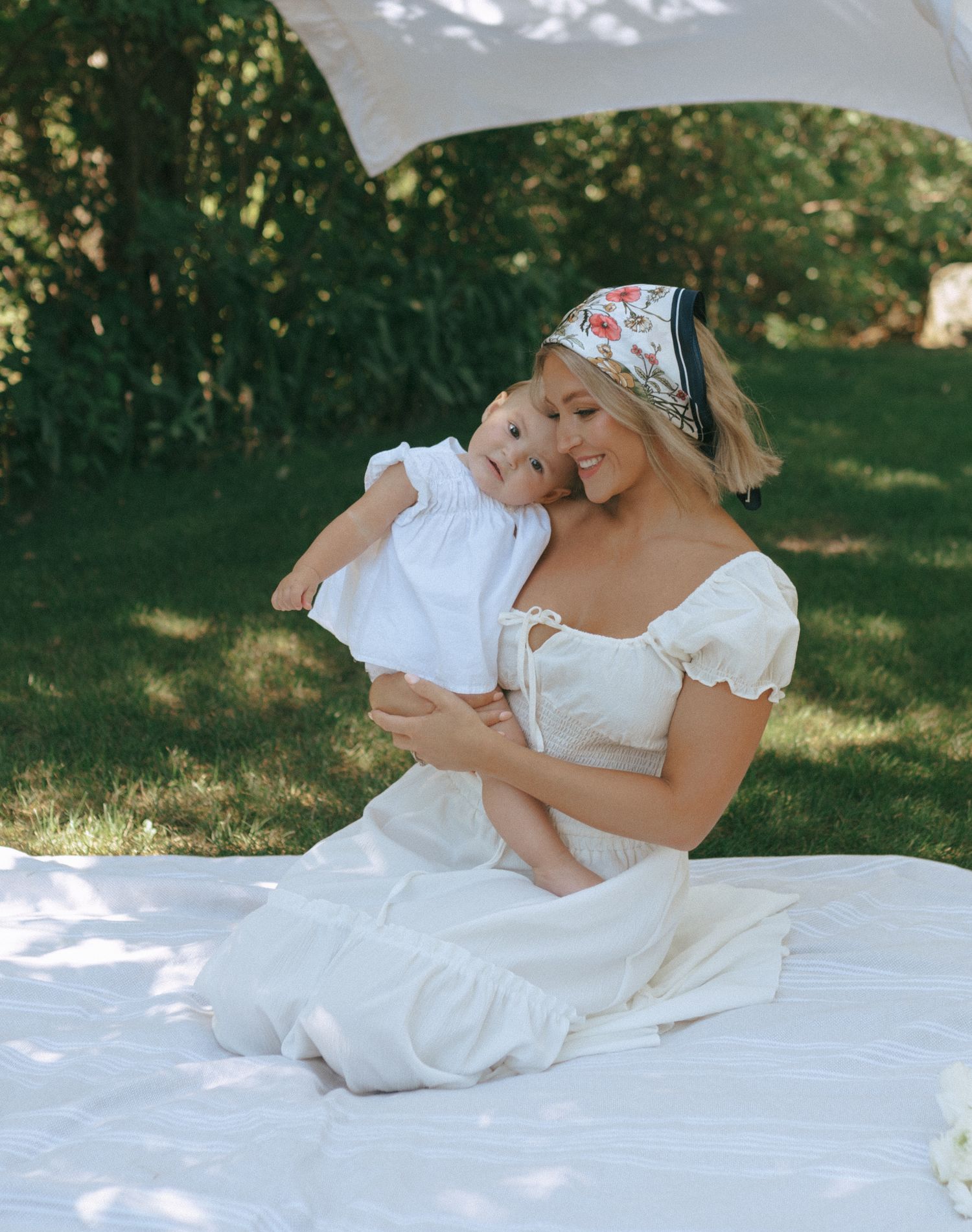 Mother and baby share intimate moments on white blanket during outdoor garden photoshoot.