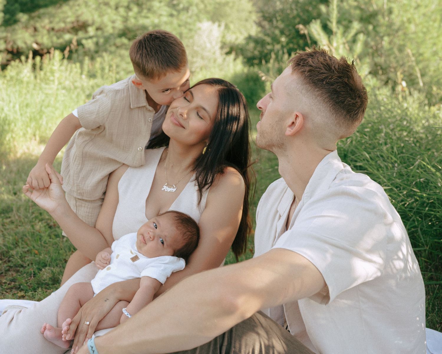 Family in white and cream outfits pose together outdoors in natural sunlight.