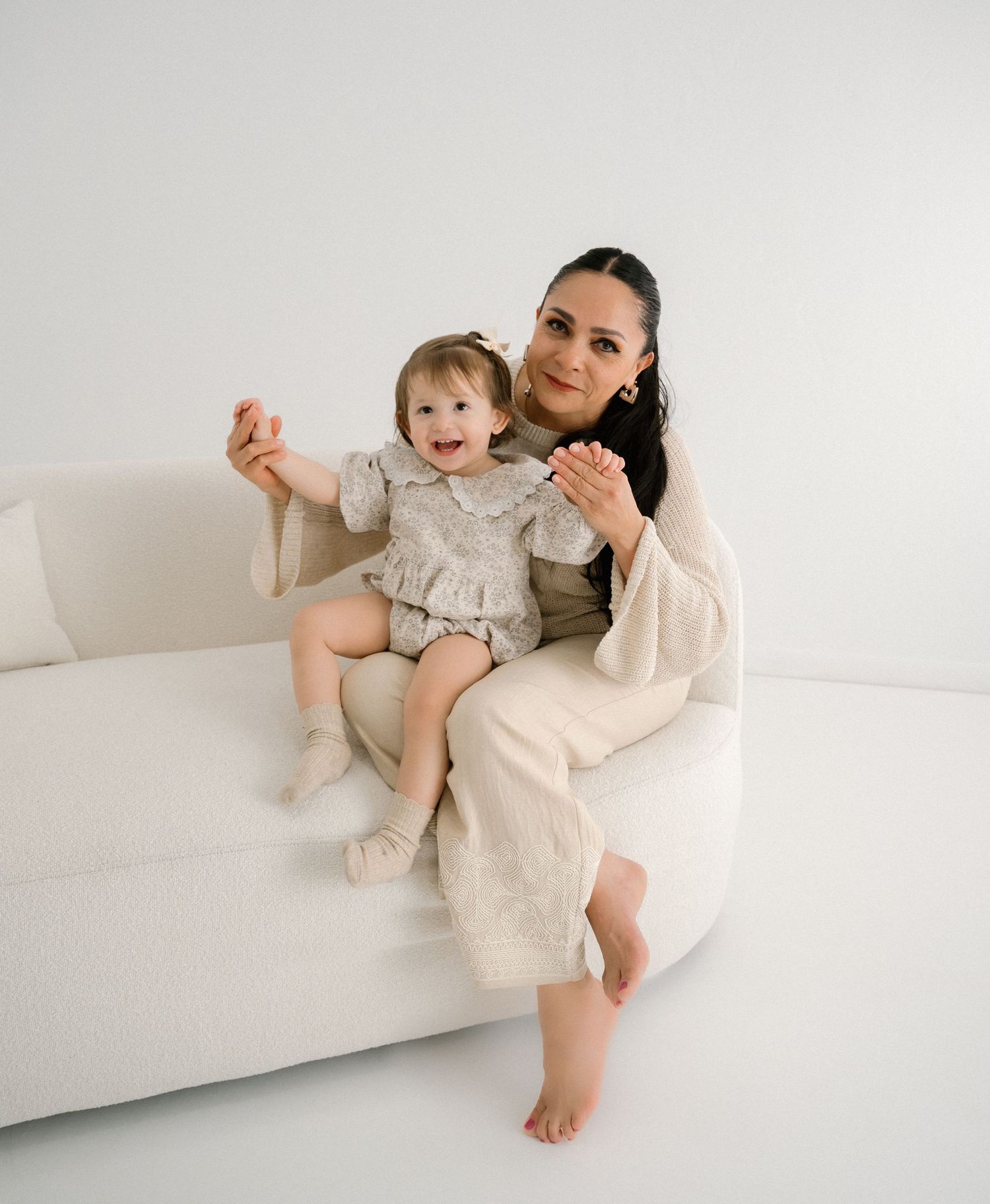 Candid moments of parent and toddler lounging together on white sofa in light-colored clothing.