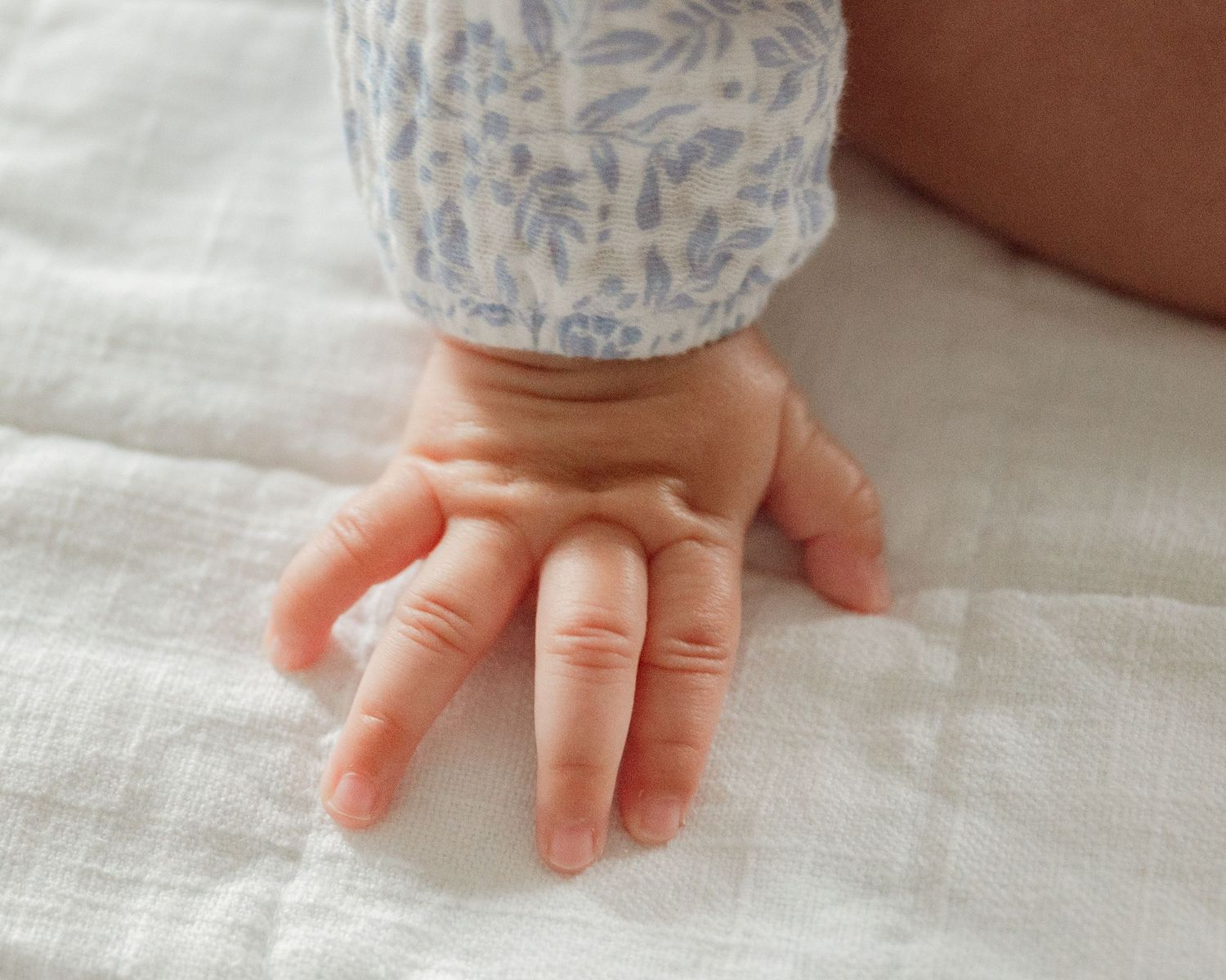Close-up shots of tiny baby hands touching white linen fabric.