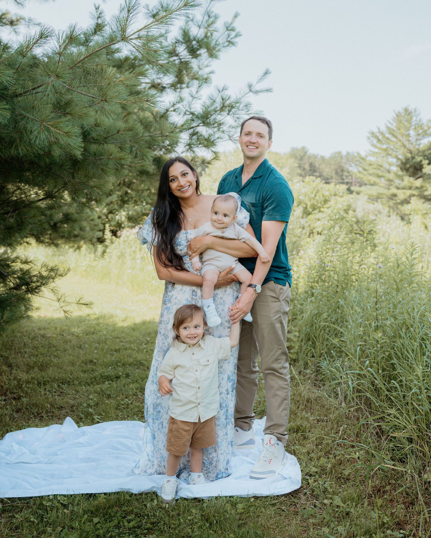 A family sits together on a picnic blanket in a sunny meadow with tall grass.