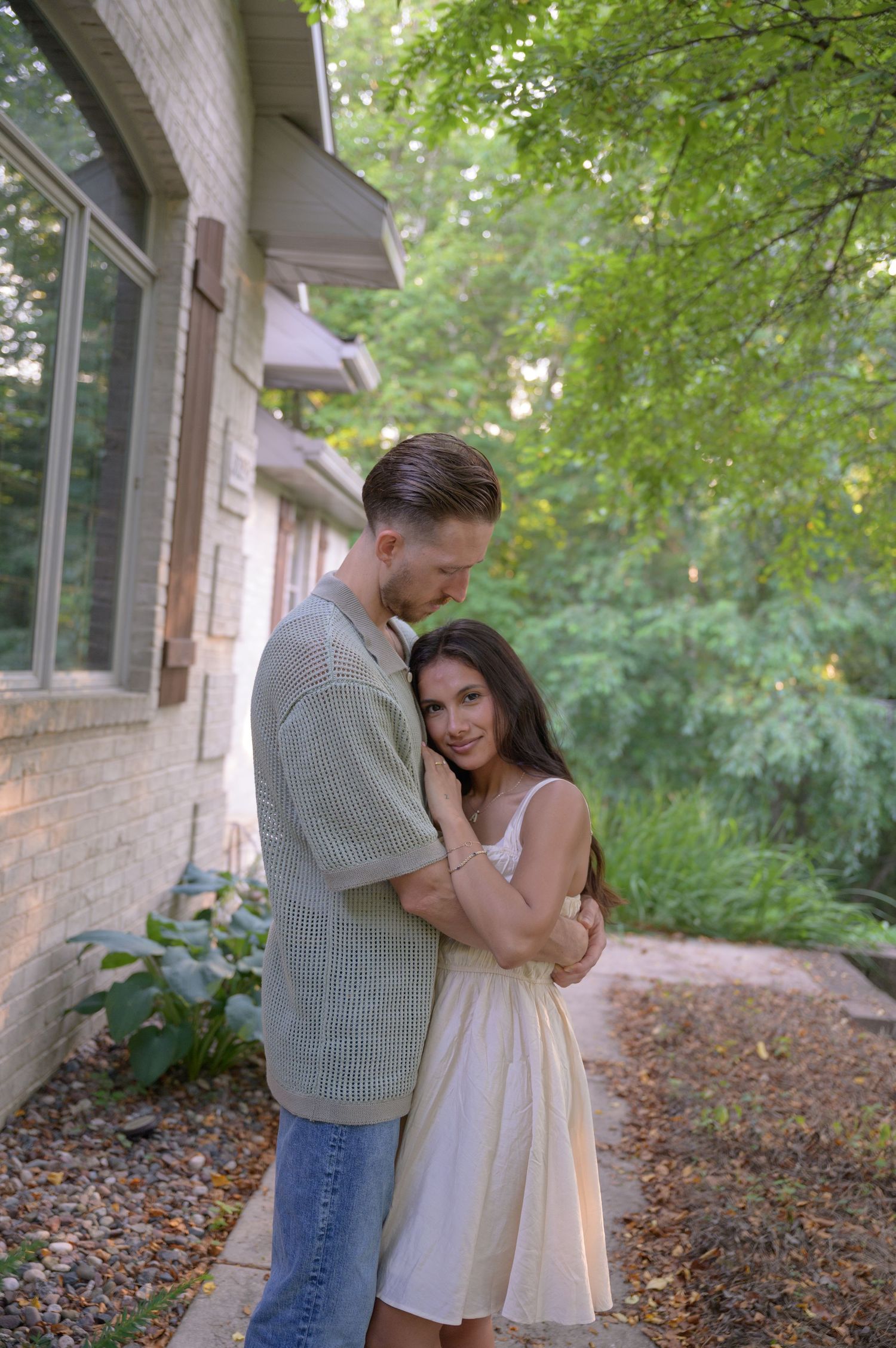 Romantic couple embracing outside brick house with green foliage. Appleton, Green Bay & Kaukauna