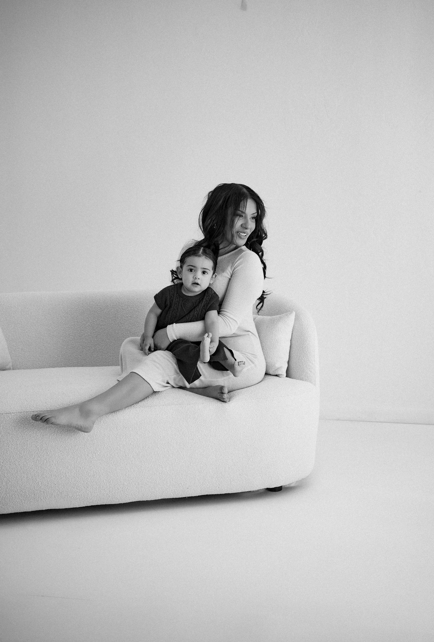 Black and white portrait of family members lounging together on a modern white sofa.