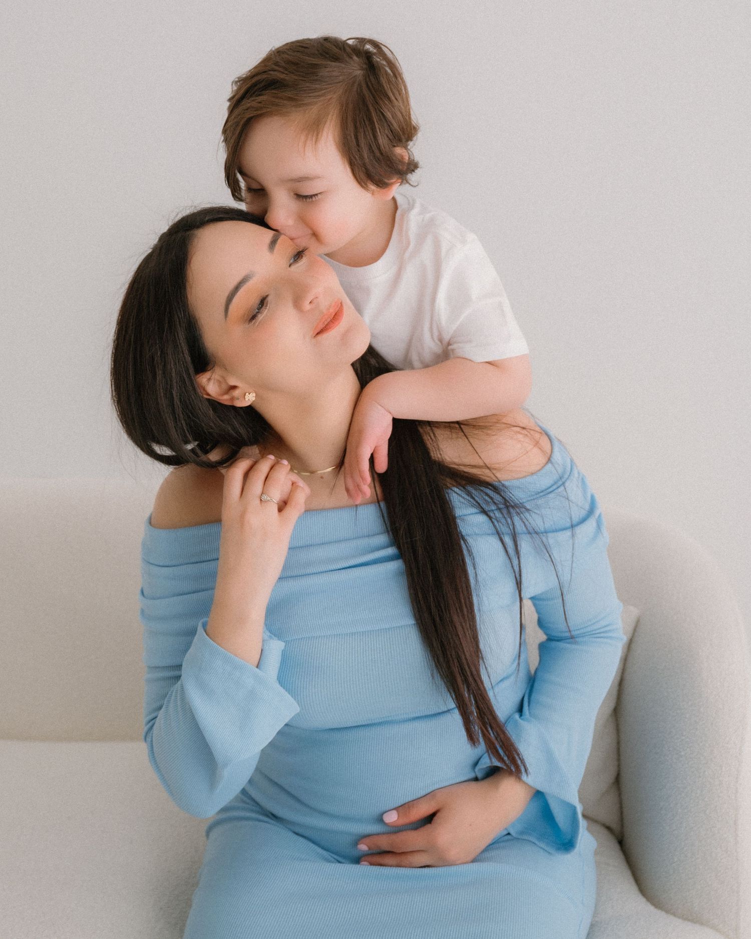 A parent and baby share tender moments together in a studio against a white wall.