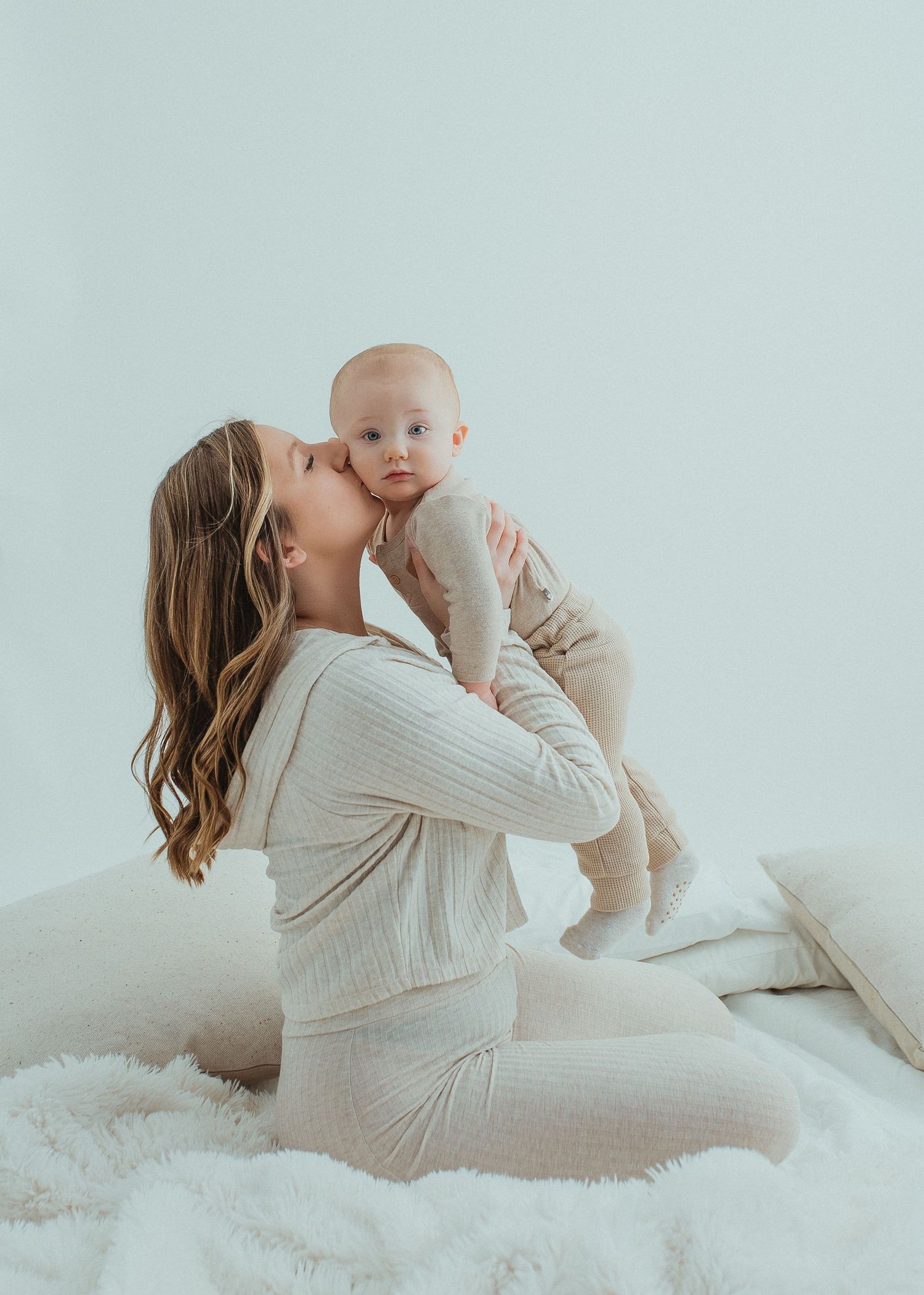 Soft minimalist portrait session showing tender moments between parent and baby on light background.