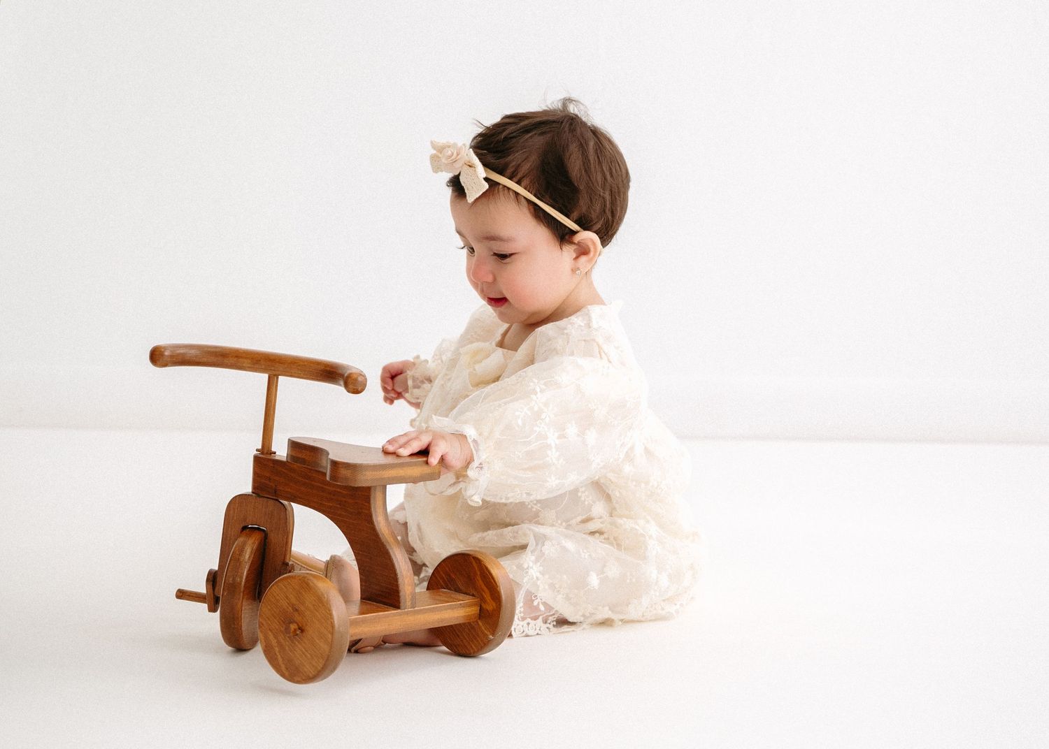 Infant in vintage dress exploring wooden toy on white backdrop. Appleton, Green Bay & Kaukauna