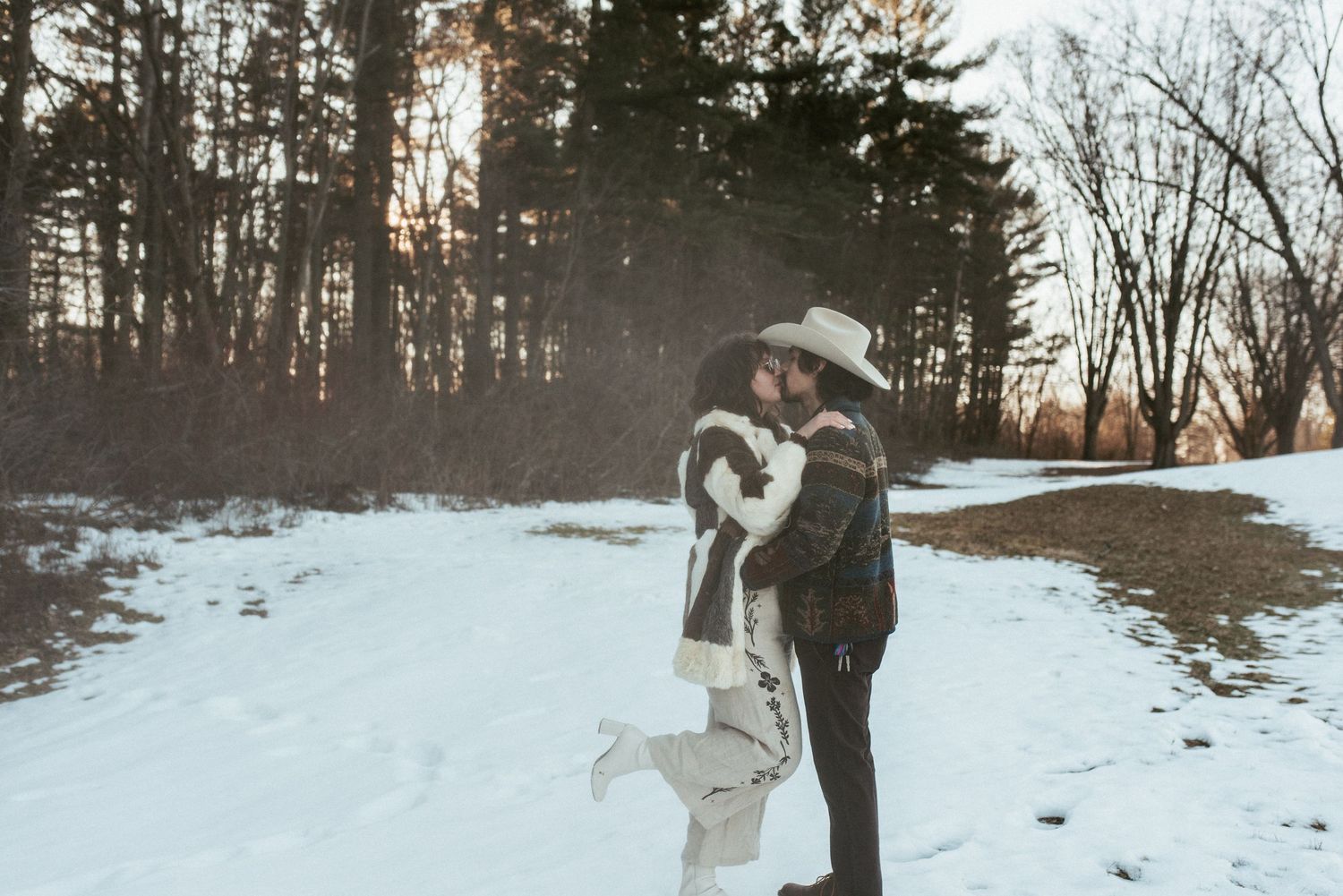 A romantic winter scene with snow-covered ground and tall evergreen trees in the background.