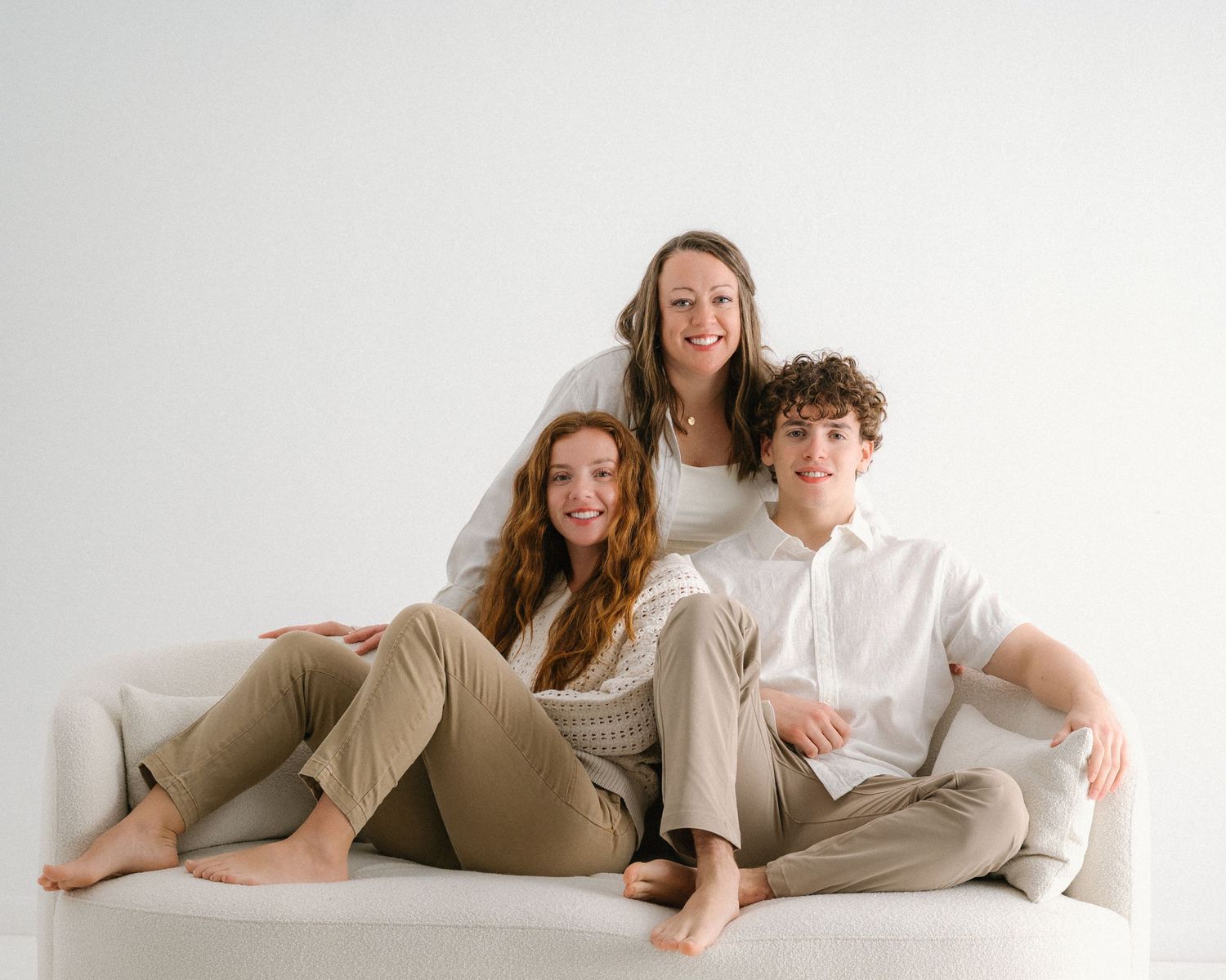 Relaxed family portrait with everyone wearing neutral colors on a white couch.