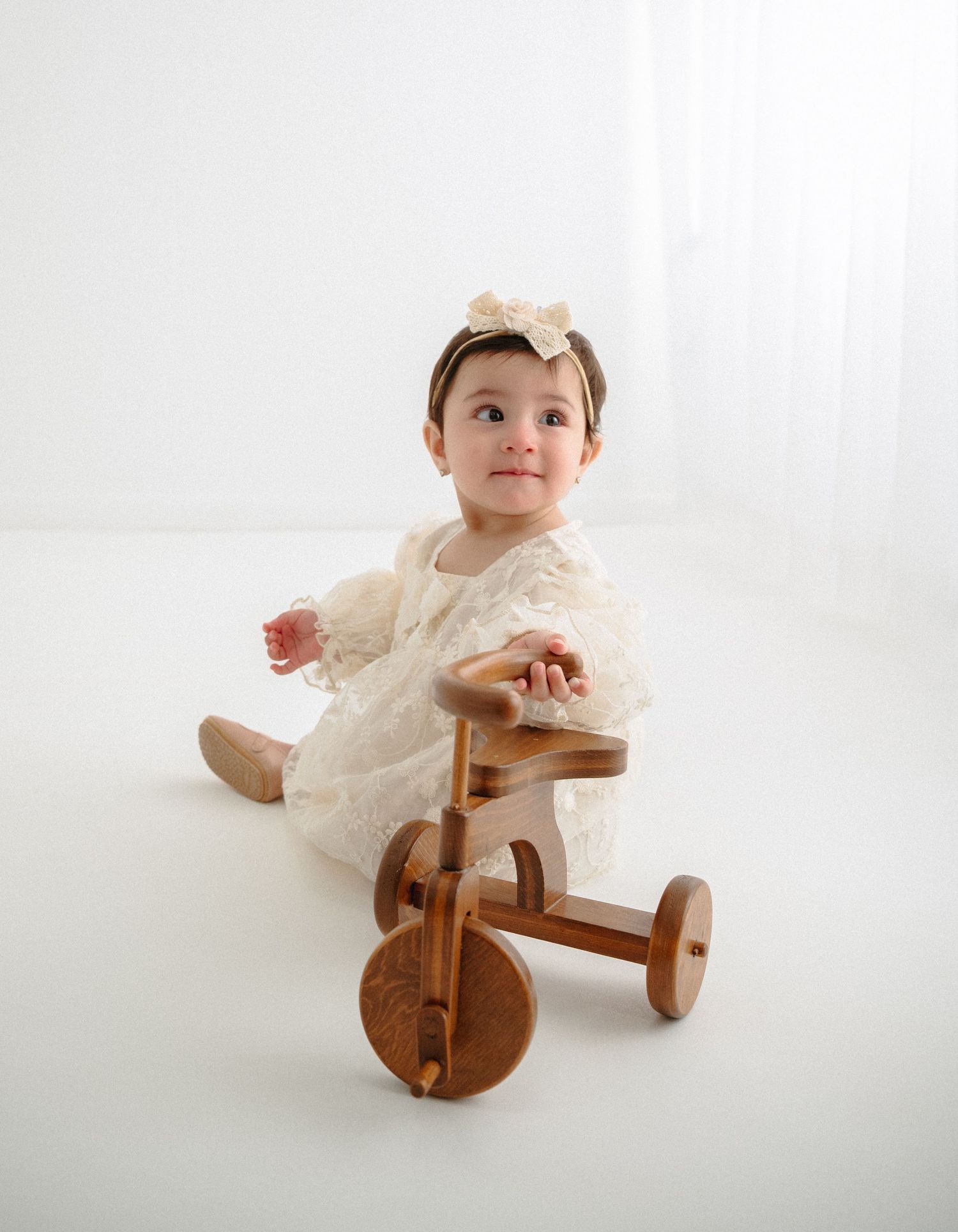 Baby dressed in cream lace dress sitting on wooden rocking horse toy. Appleton, Green Bay & Kaukauna