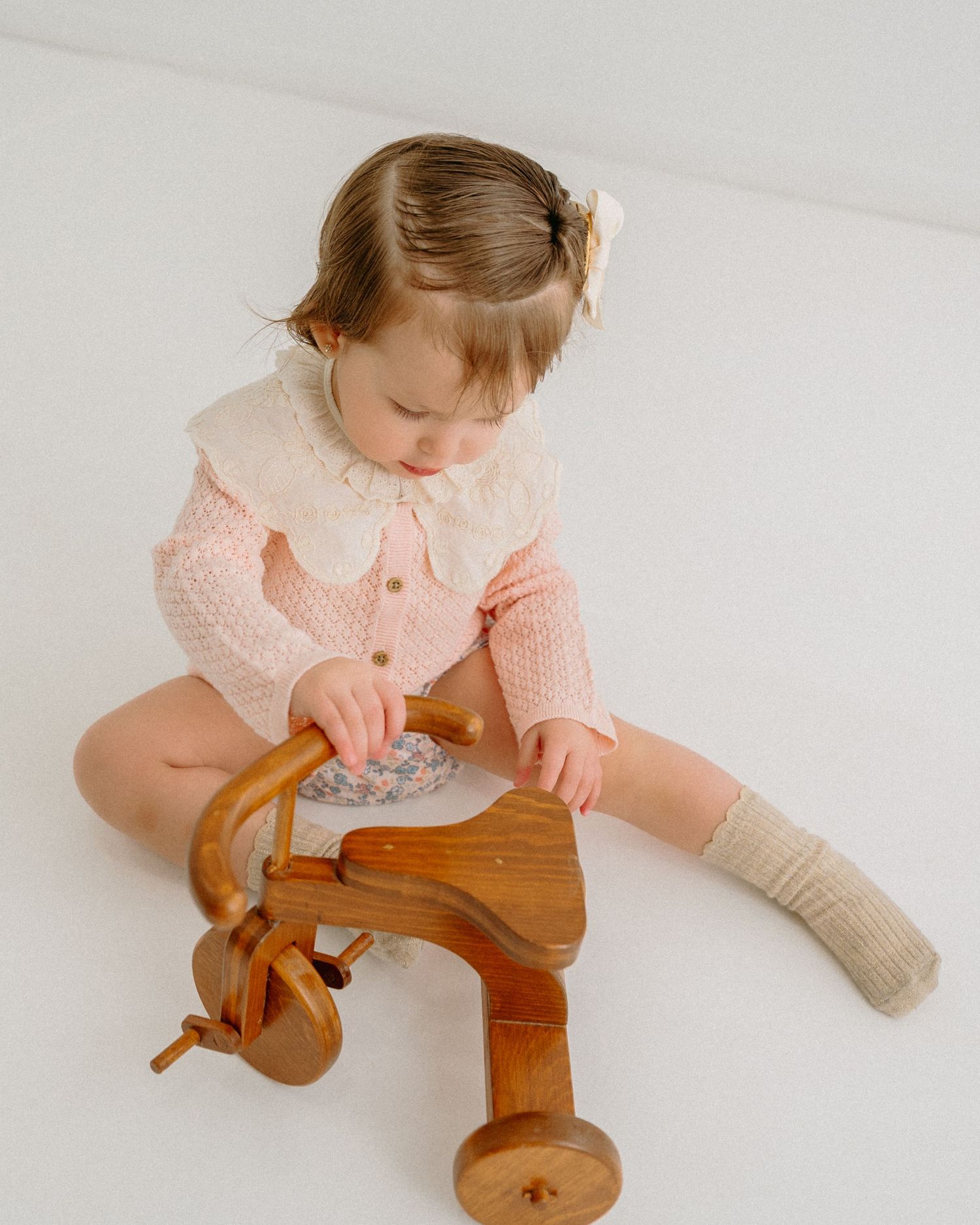 Small child in pink sweater exploring a wooden toy while sitting on white background. Appleton, Green Bay & Kaukauna