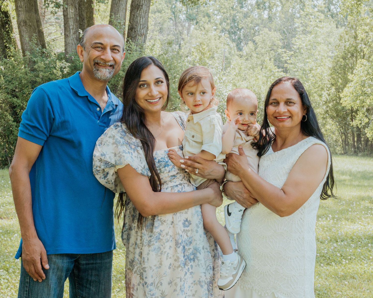 A multi-generational family gathering poses for photos in a sunlit forest setting.