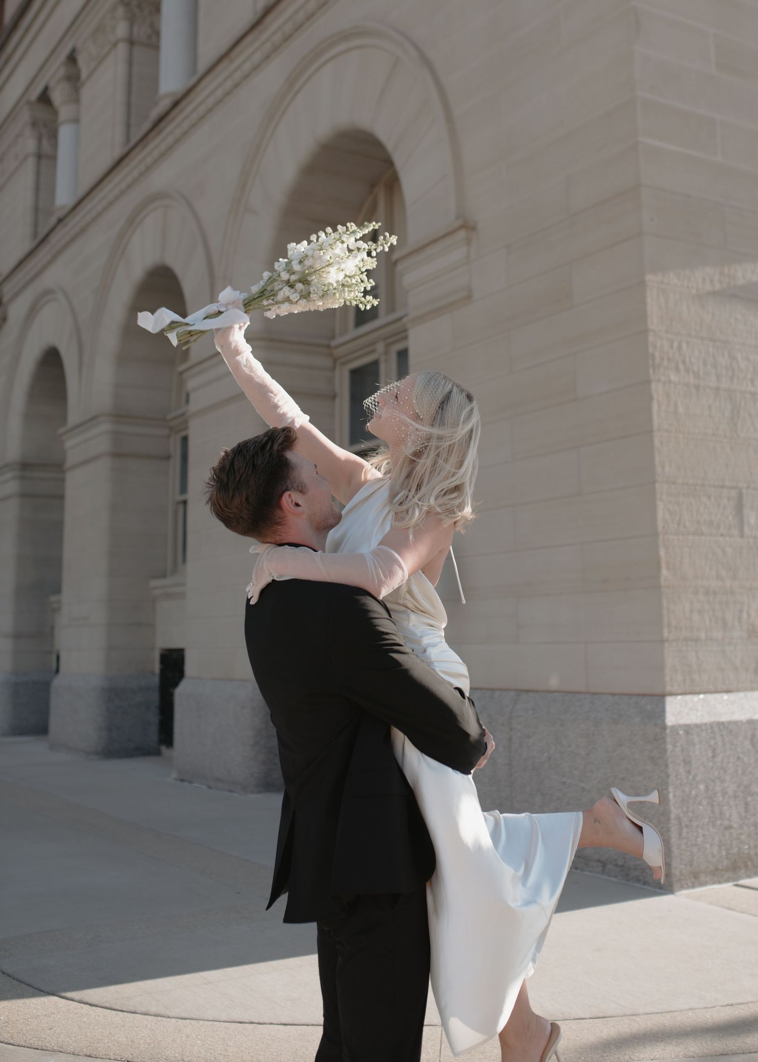 Elegant wedding couple dancing and twirling together in front of a classic stone building.