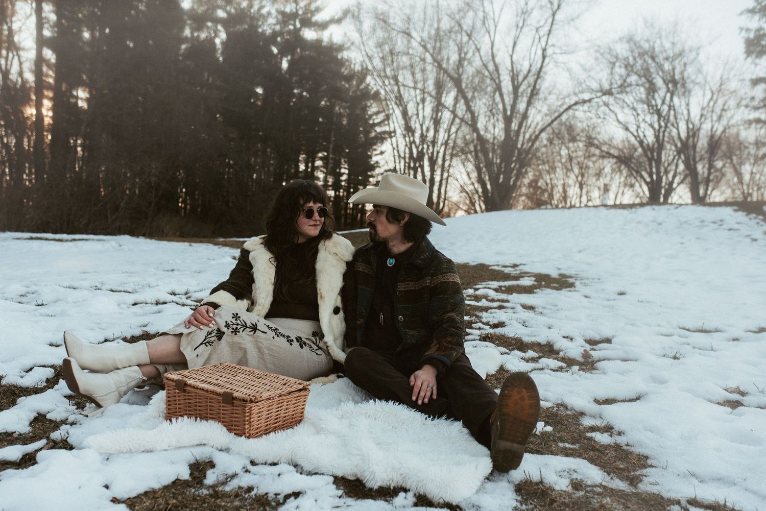 Couple sitting together in snowy winter landscape with picnic basket and blanket during romantic afternoon date. Appleton, Green Bay & Kauka