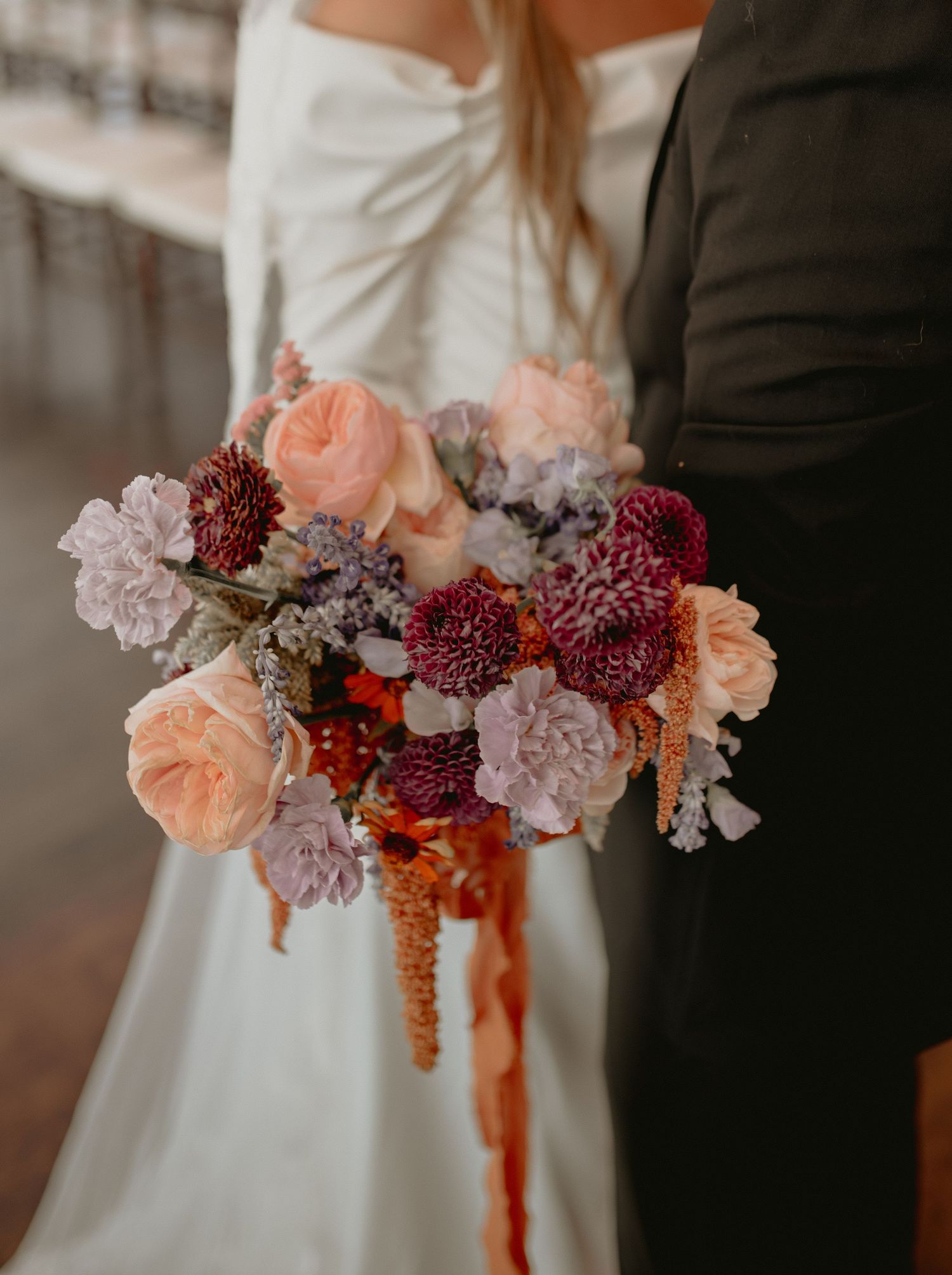 Detailed shot of romantic wedding bouquet featuring pink and burgundy flowers with trailing ribbons.