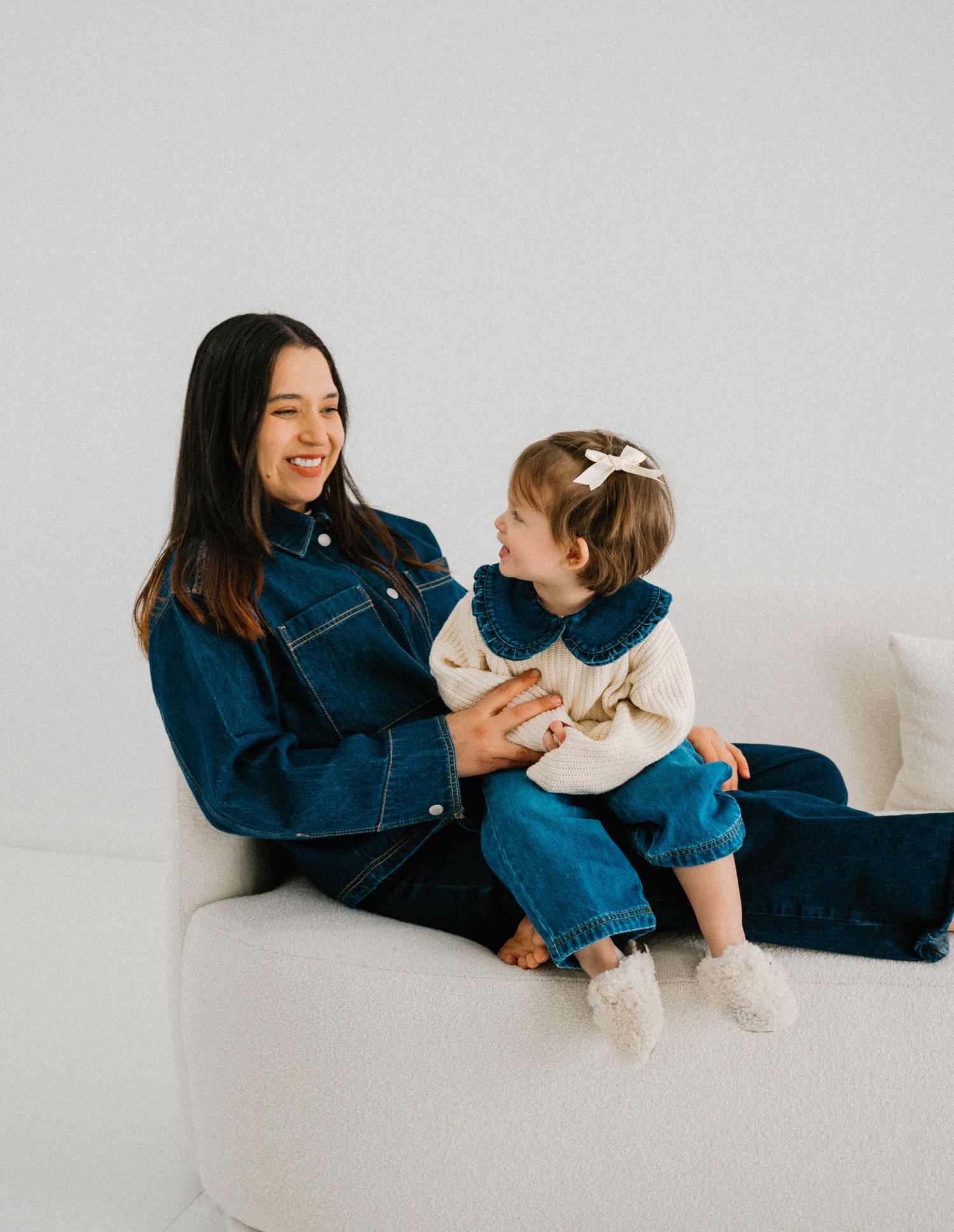 Joyful playtime moments between parent in denim and child on white furniture.