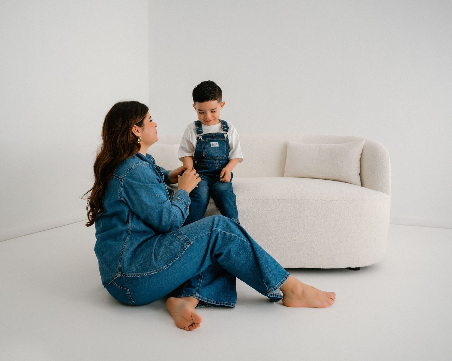 Mother and child in coordinated denim outfits pose together in a bright white studio setting.