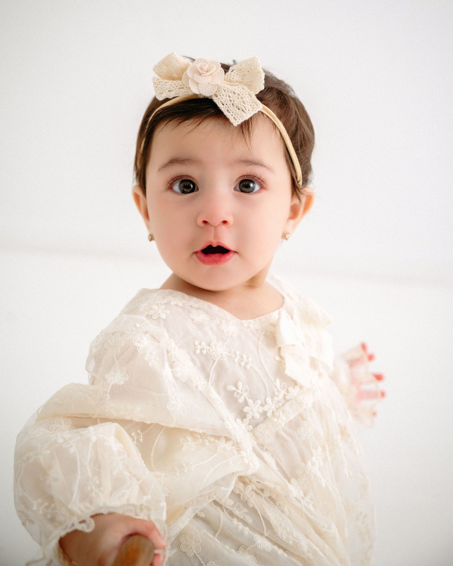 Baby wearing lace dress and bow headband against white background. Appleton, Green Bay & Kaukauna