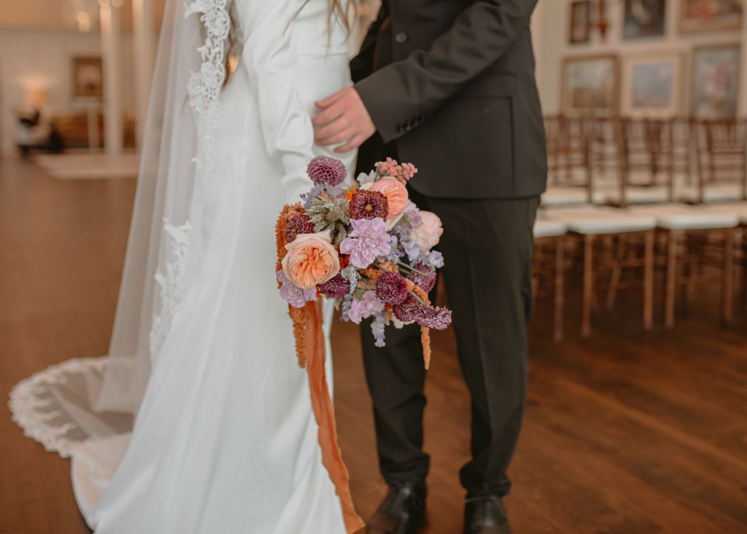 A couple embraces during their first look in an elegant venue with wooden floors.