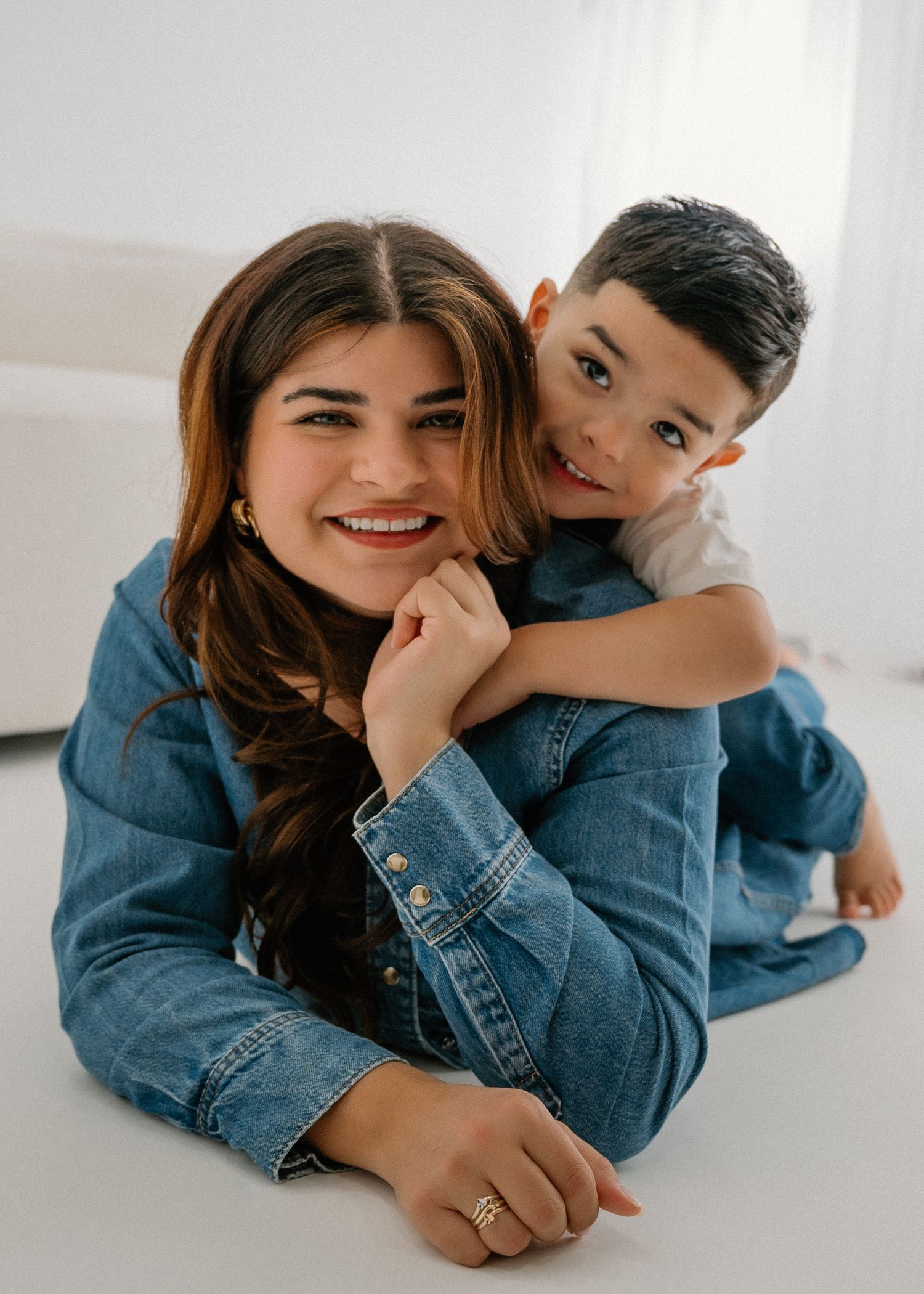 Family members in matching denim outfits share playful moments while lying on the floor in a minimalist setting.