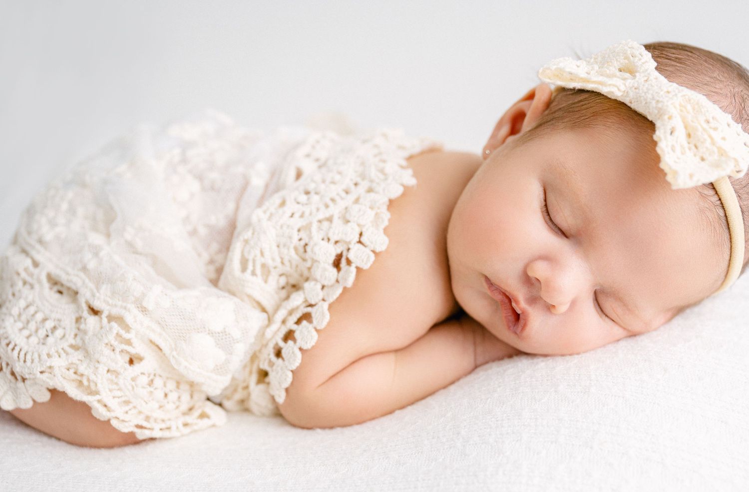 Sleeping newborn wrapped in delicate lace on white fabric. Appleton, Green Bay & Kaukauna