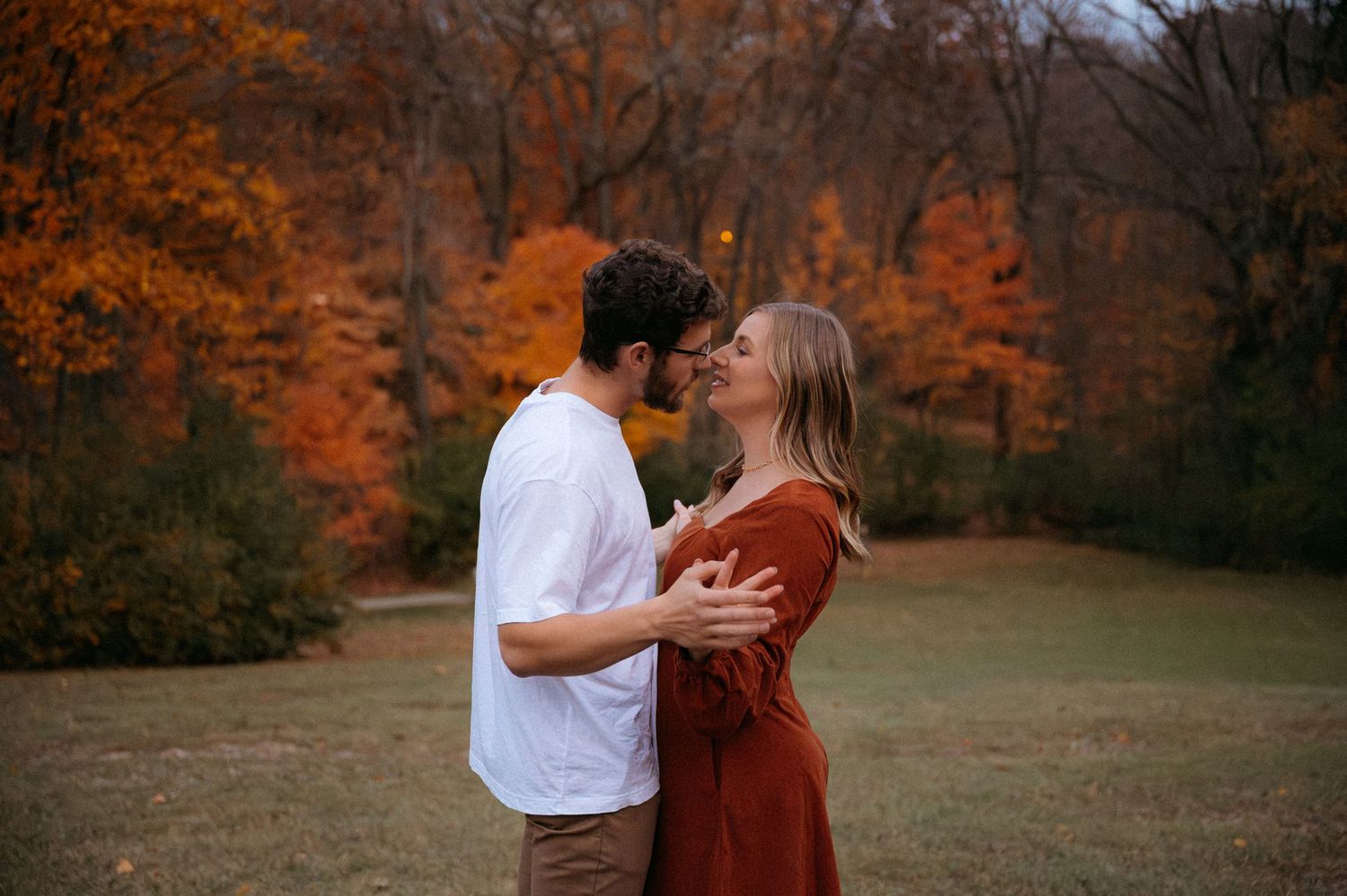 A romantic couple embraces in a field surrounded by vibrant autumn foliage on a fall afternoon. Appleton, Green Bay & Kaukauna